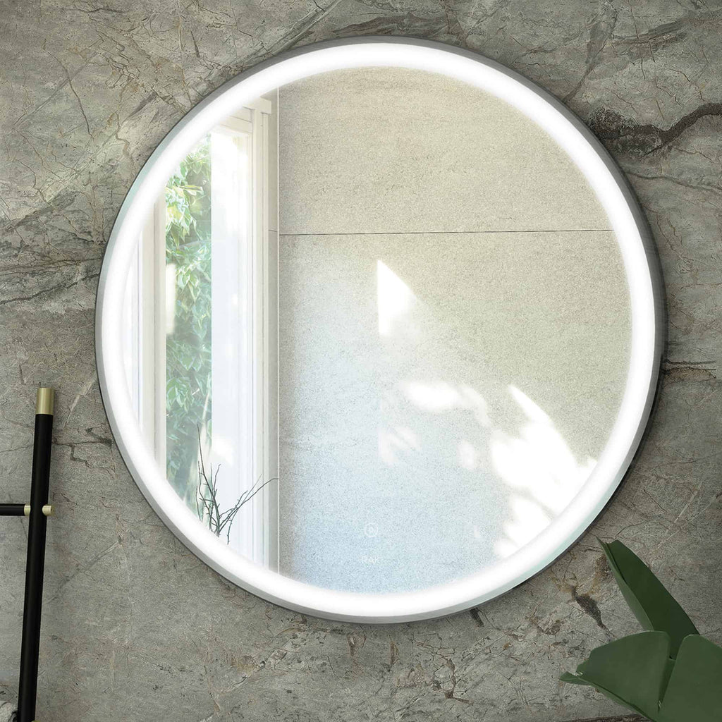 Illuminated round bathroom mirror with LED lighting mounted on a marble wall, reflecting a bright window and green plants, ideal for modern bathroom decor.