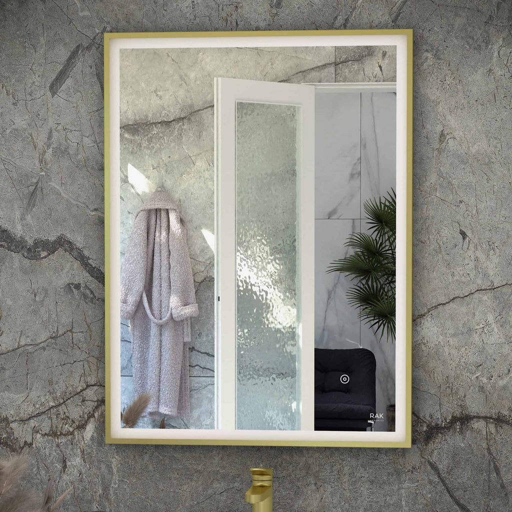 Contemporary bathroom mirror with gold frame on textured marble wall, featuring a cosy robe hook, lush green plant and modern shower area, enhancing a stylish and functional bathroom space.