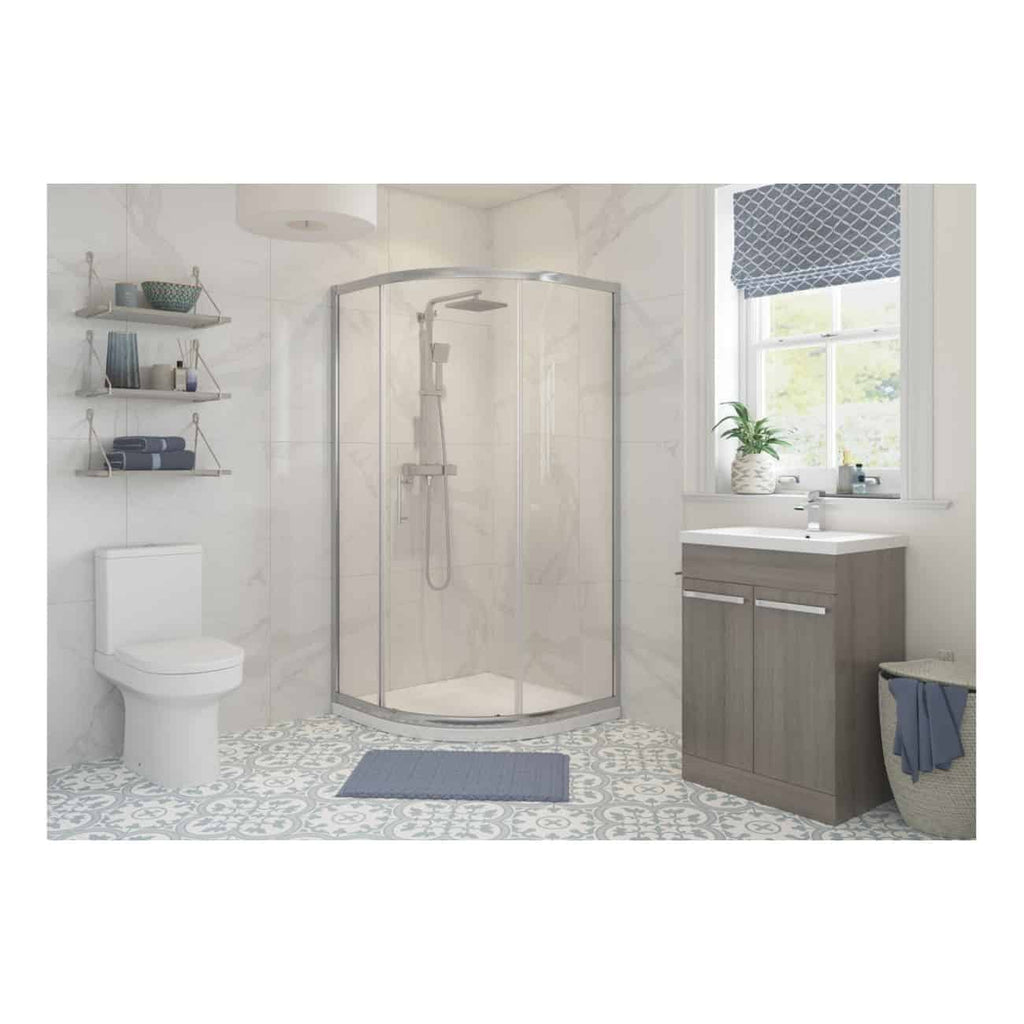 Bright modern bathroom with a corner shower enclosure, white toilet, grey vanity unit with sink, decorative patterned floor tiles, and natural light from a window with a blue Roman blind.