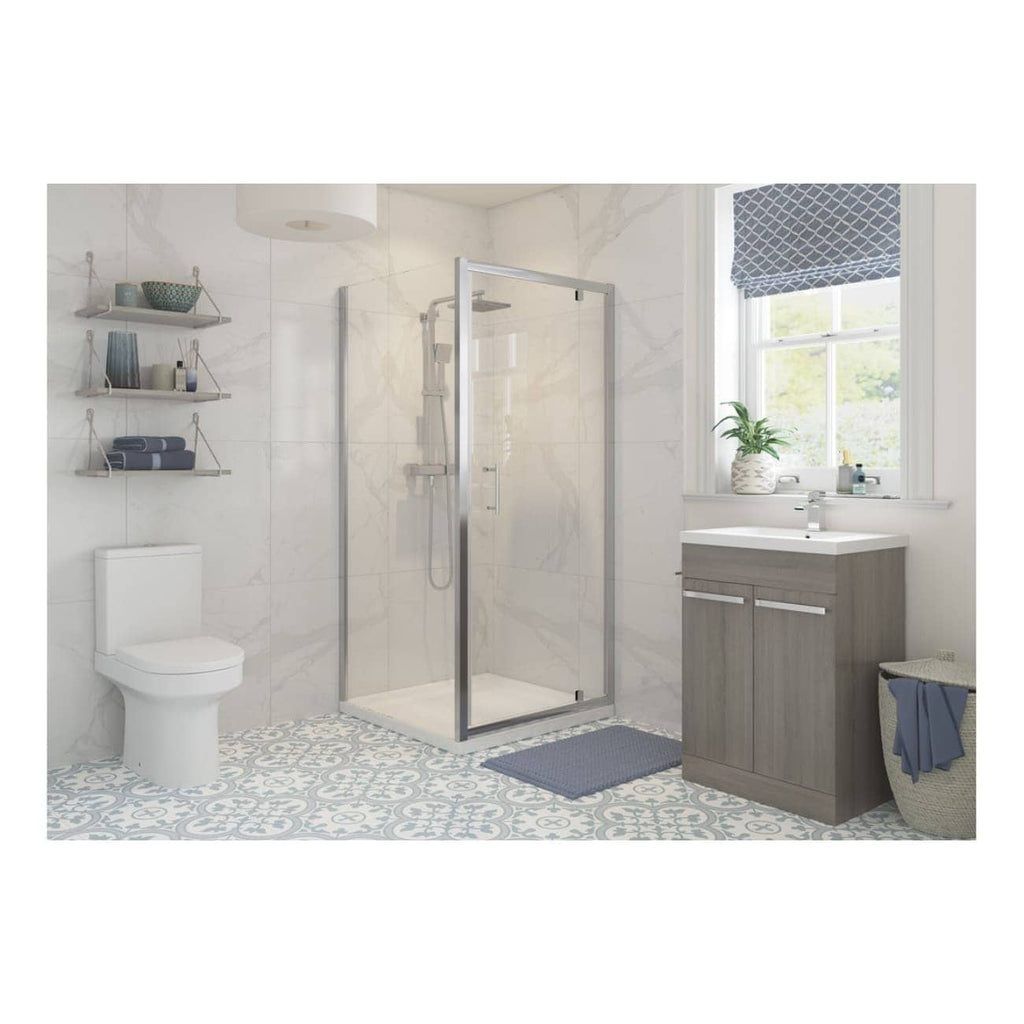 Bright modern bathroom featuring a walk-in glass shower, white toilet, grey vanity unit, and decorative patterned floor tiles, with natural light from a side window.