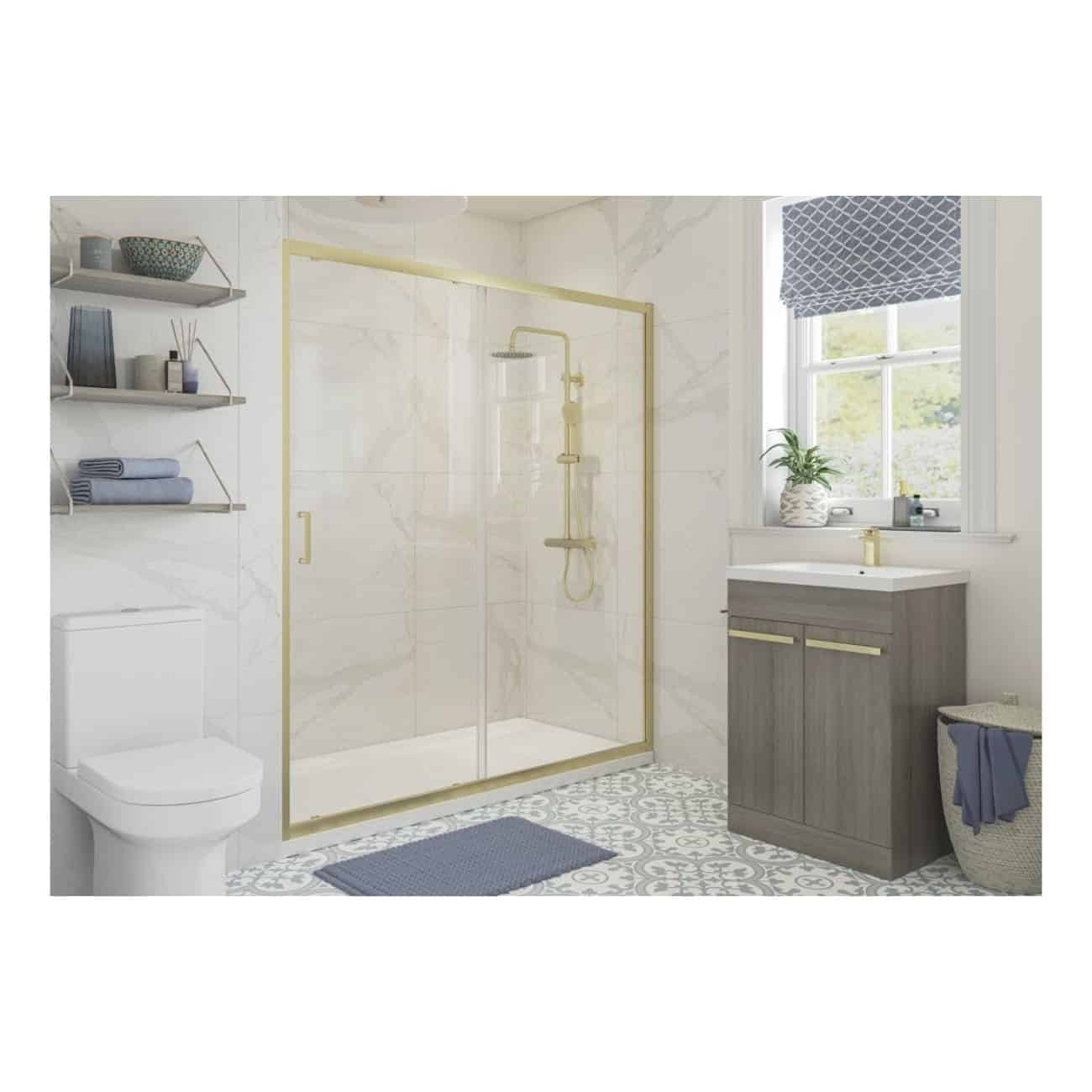 Bright modern bathroom featuring a walk-in shower with gold trim, grey vanity with gold accents, white marble walls, patterned floor tiles, and a large window with a blue Roman blind.