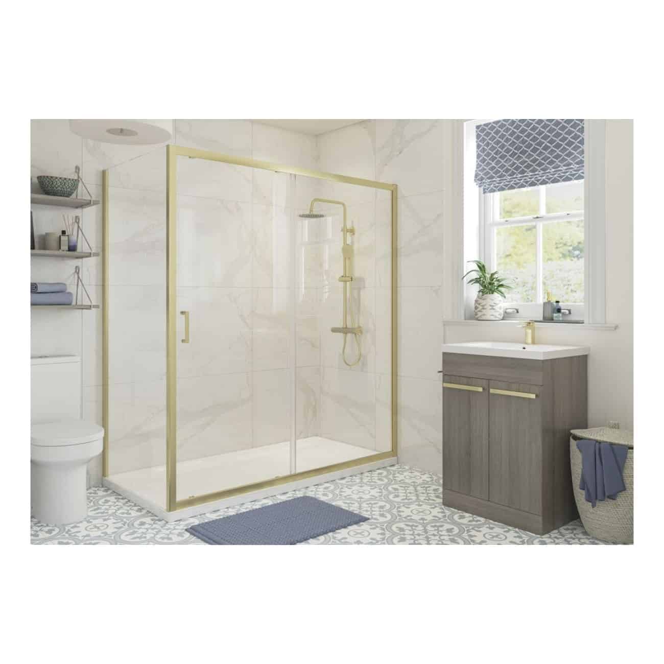 Bright modern bathroom featuring a glass shower enclosure with gold trim, contemporary grey vanity with gold accents, patterned tiled floor, and a large window with a blue Roman blind, creating a stylish and functional space.