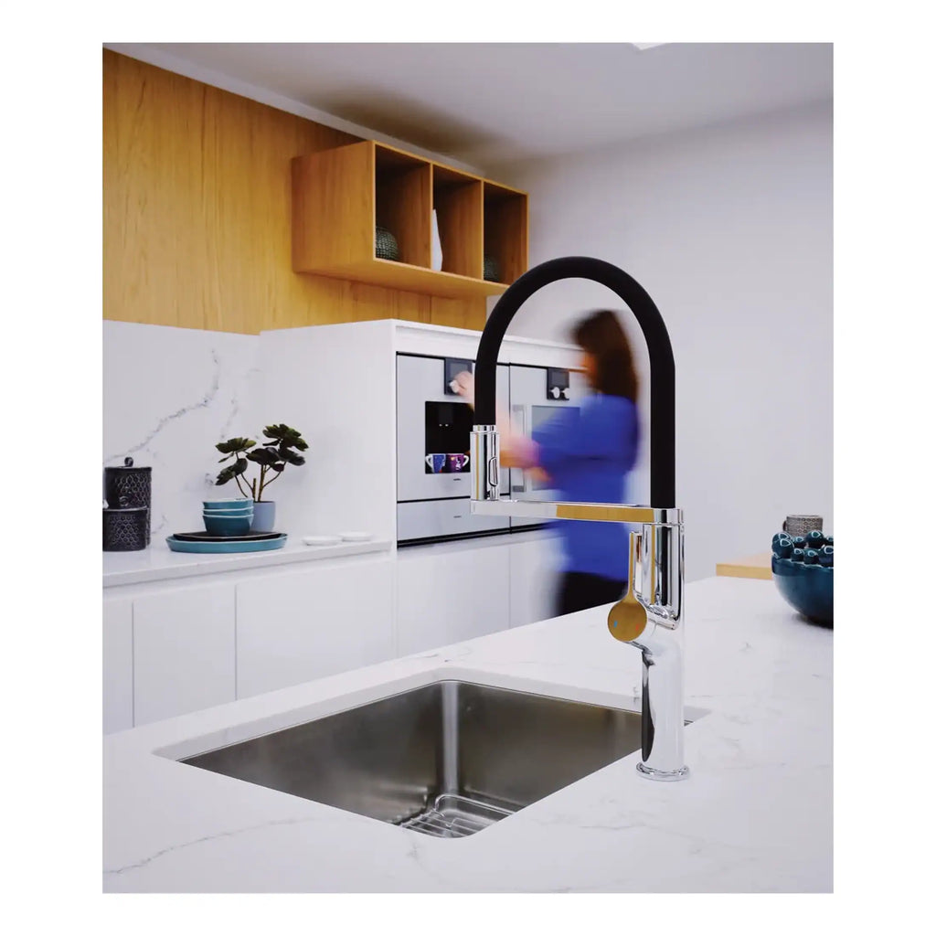 Sleek black and chrome kitchen sink tap with modern design, installed over a stainless steel sink in a contemporary kitchen featuring white marble countertops and minimalist decor.