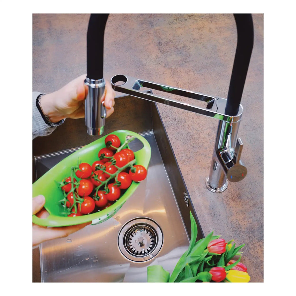 Bright modern kitchen stainless steel single basin sink with chrome finish, high-arc kitchen tap, and a hand holding a green bowl of cherry tomatoes, surrounded by fresh tulips, showcasing stylish kitchen spaces.