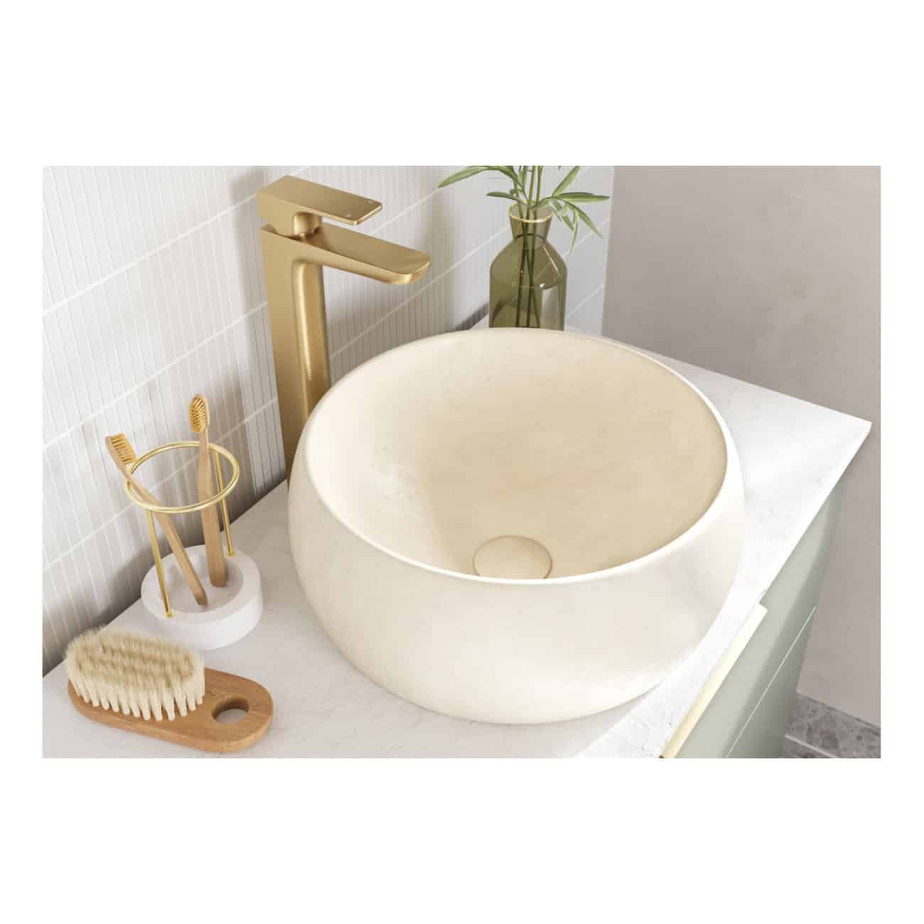 Sleek beige stone bathroom vessel sink with gold fixtures, complemented by toothbrush holder, bath brush, and a minimalist decor with a green vase, creating a luxurious bathroom aesthetic.