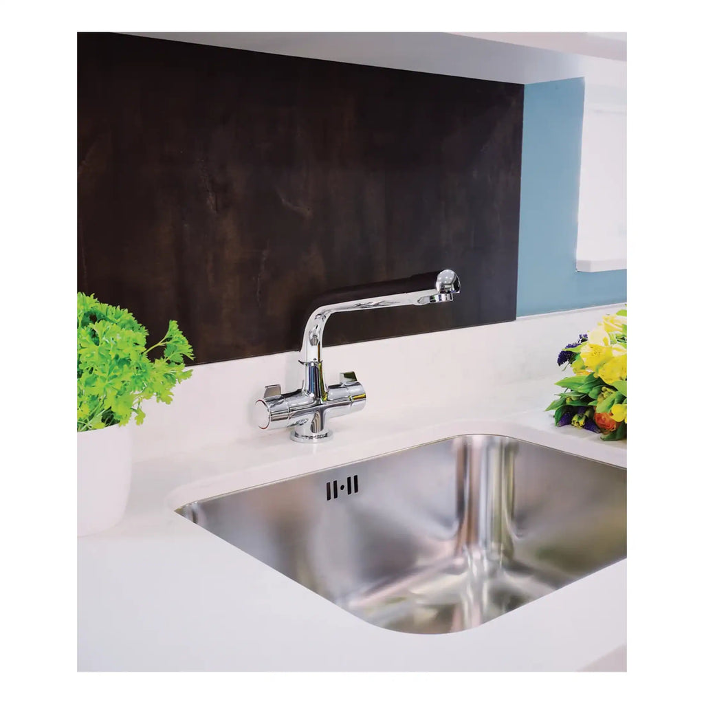 Shiny stainless steel kitchen sink with modern chrome faucet, white countertop, green plant, and colourful flowers on a kitchen workspace.