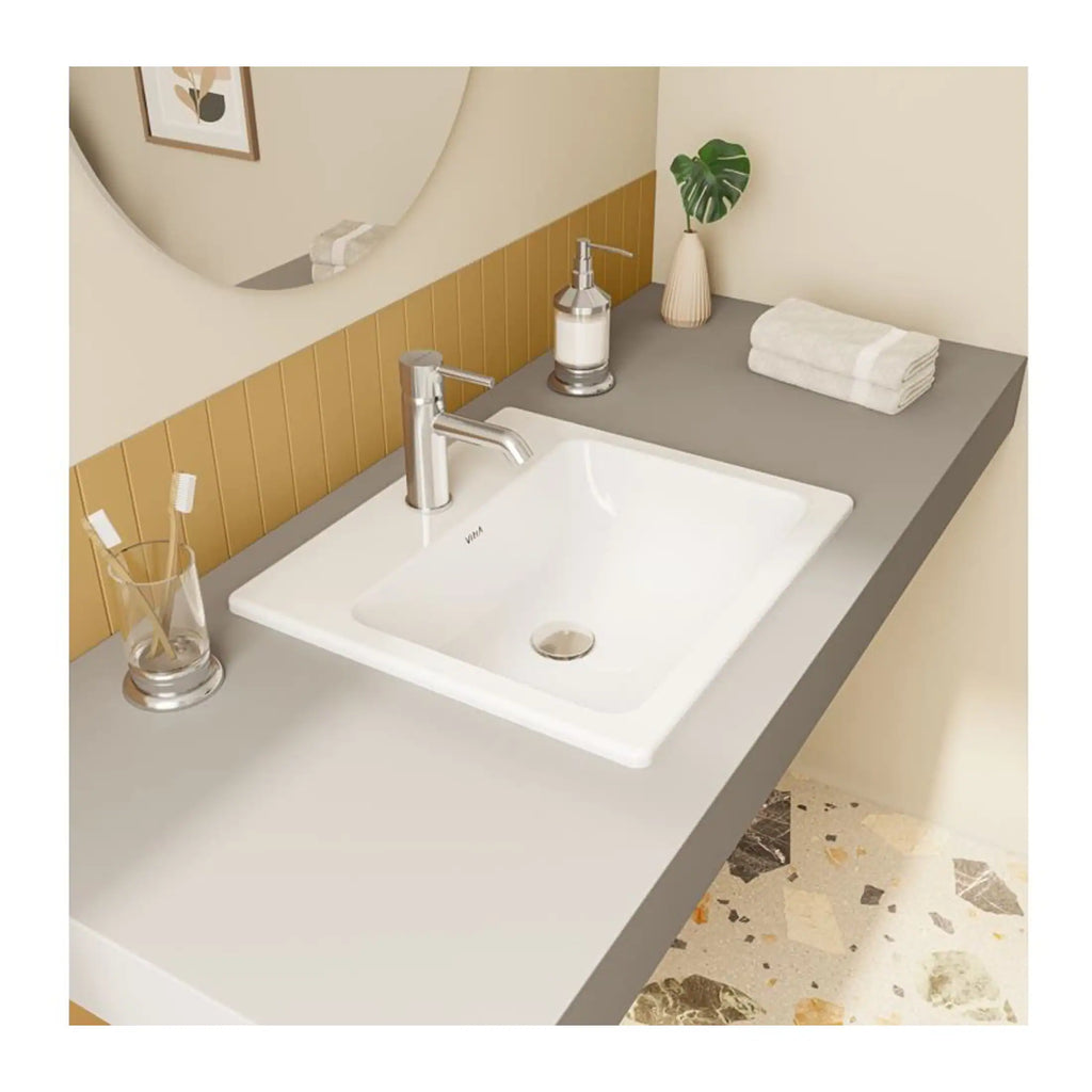 Bright modern bathroom sink with sleek chrome faucet, white soap dispenser, neatly folded towels, and a decorative plant on a minimalist grey countertop, featuring a large mirror and stylish beige wall decor.
