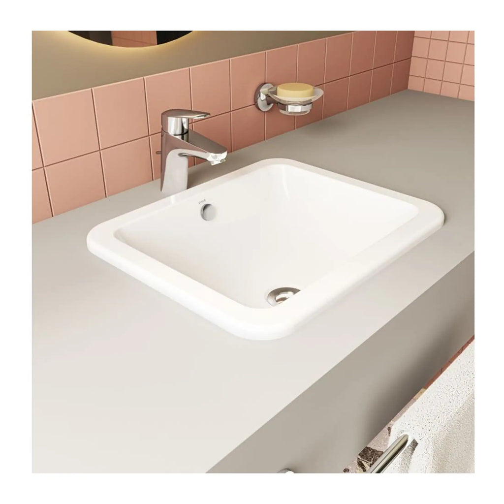 Bright white modern bathroom sink with sleek chrome faucet, set into a smooth countertop with pink tiled backsplash and accessories for stylish and functional bathroom design.