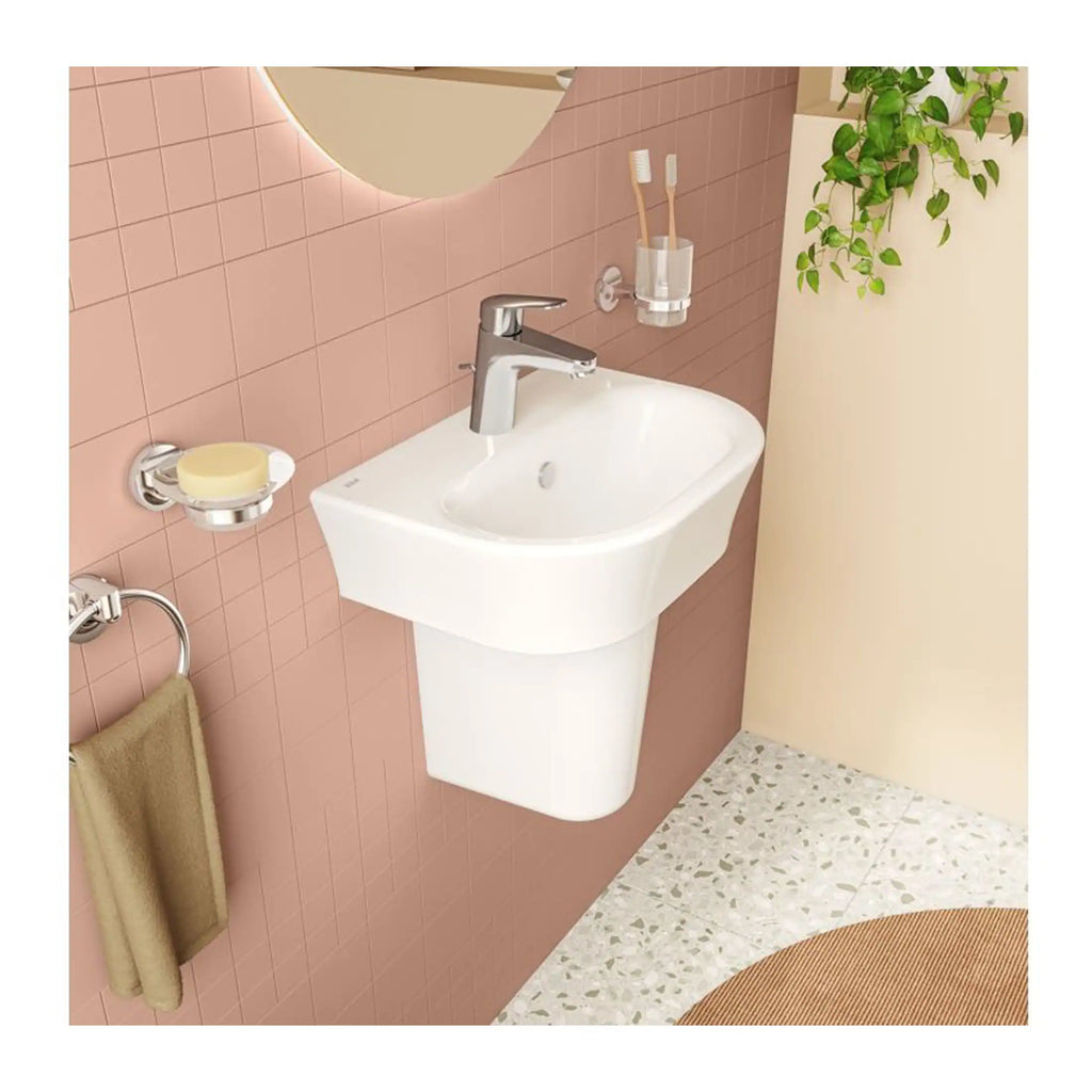 Modern wall-mounted bathroom sink with chrome faucet and pink tiled wall, featuring a round mirror, toothbrush holder, soap dish, beige towel, and green plant for stylish bathroom interior.