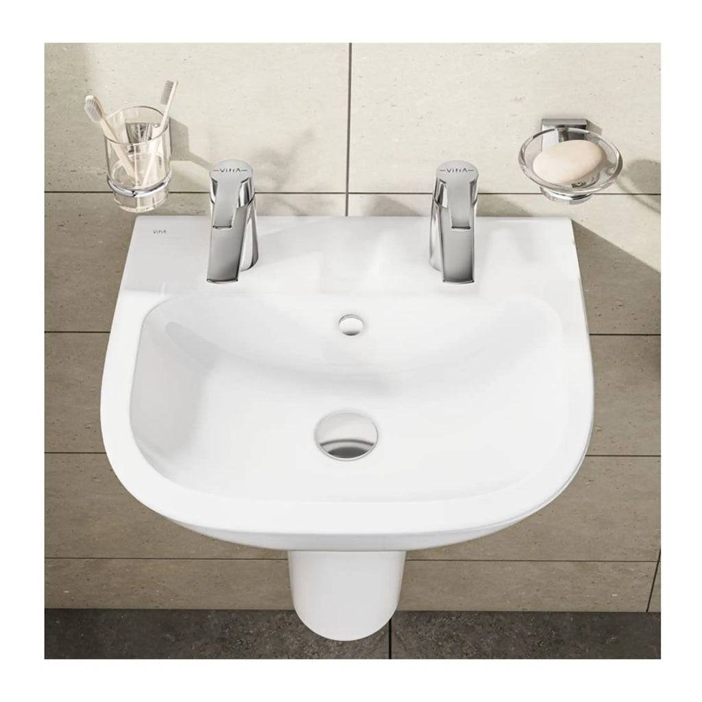 Shiny white bathroom washbasin with dual chrome taps, toothbrush holder, soap dish, and beige tiled wall background, showcasing modern bathroom fixtures and design.