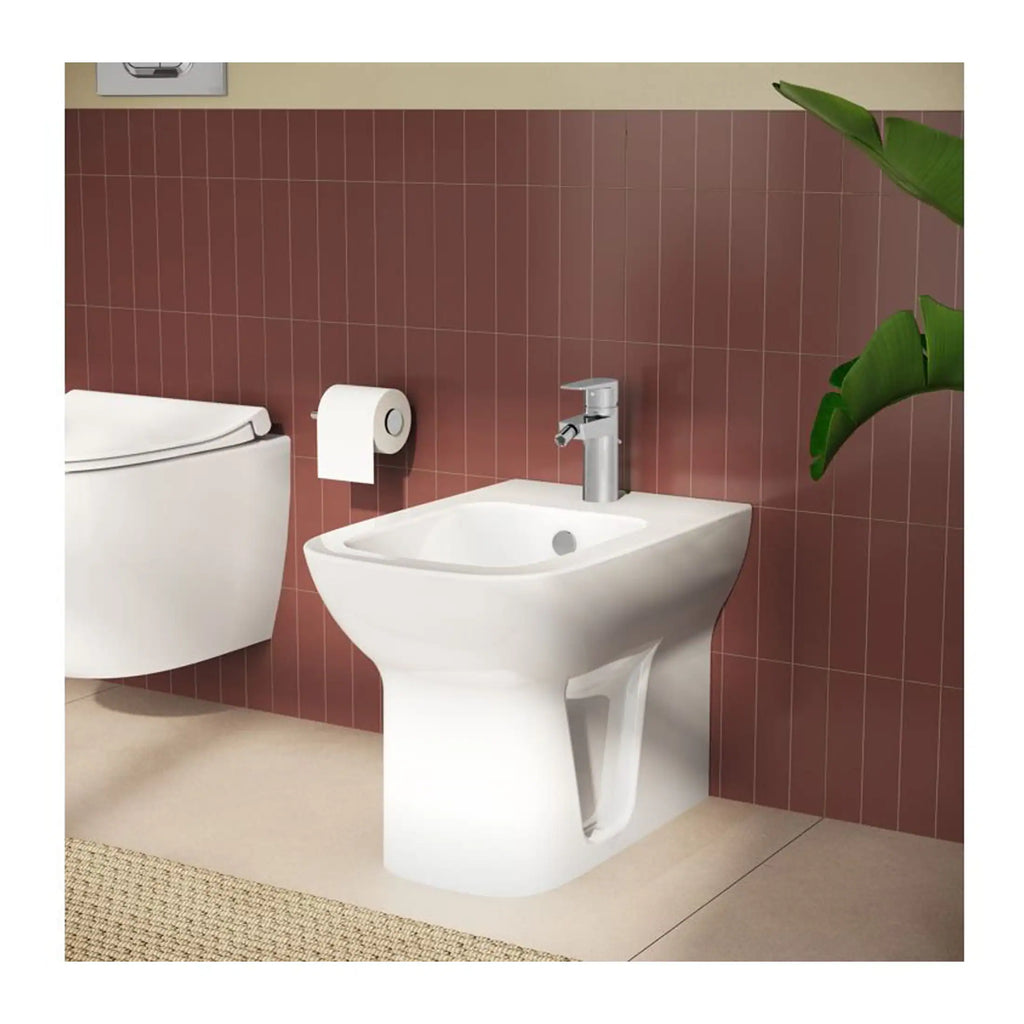 Comfortable white bathroom bidet with sleek faucet, positioned next to a modern toilet and wall-mounted toilet paper holder in a stylish bathroom setting.