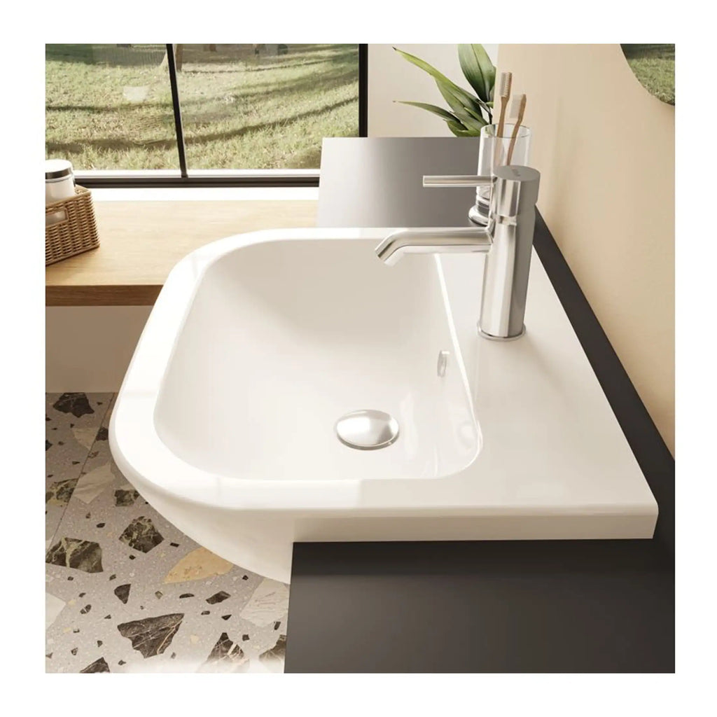 Close-up of a modern white sink with a sleek chrome tap, set in a contemporary bathroom featuring terrazzo flooring and a large window with natural light.