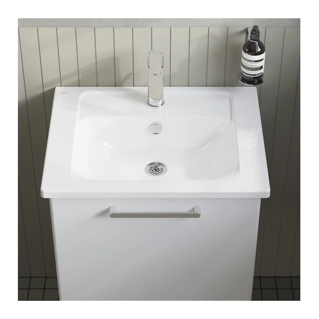 Sleek white bathroom sink with modern chrome faucet and matching cabinet, positioned against a tiled wall with a shelf holding bathroom essentials for a clean, contemporary look.