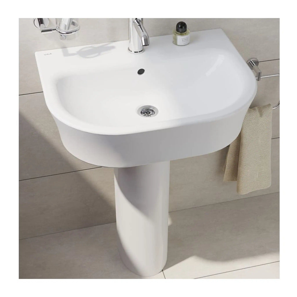 Sleek white bathroom pedestal sink with chrome fixtures and beige towel, ideal for modern bathrooms. Features a clean design with a single-handle faucet, small bottle of soap, and contemporary style.
