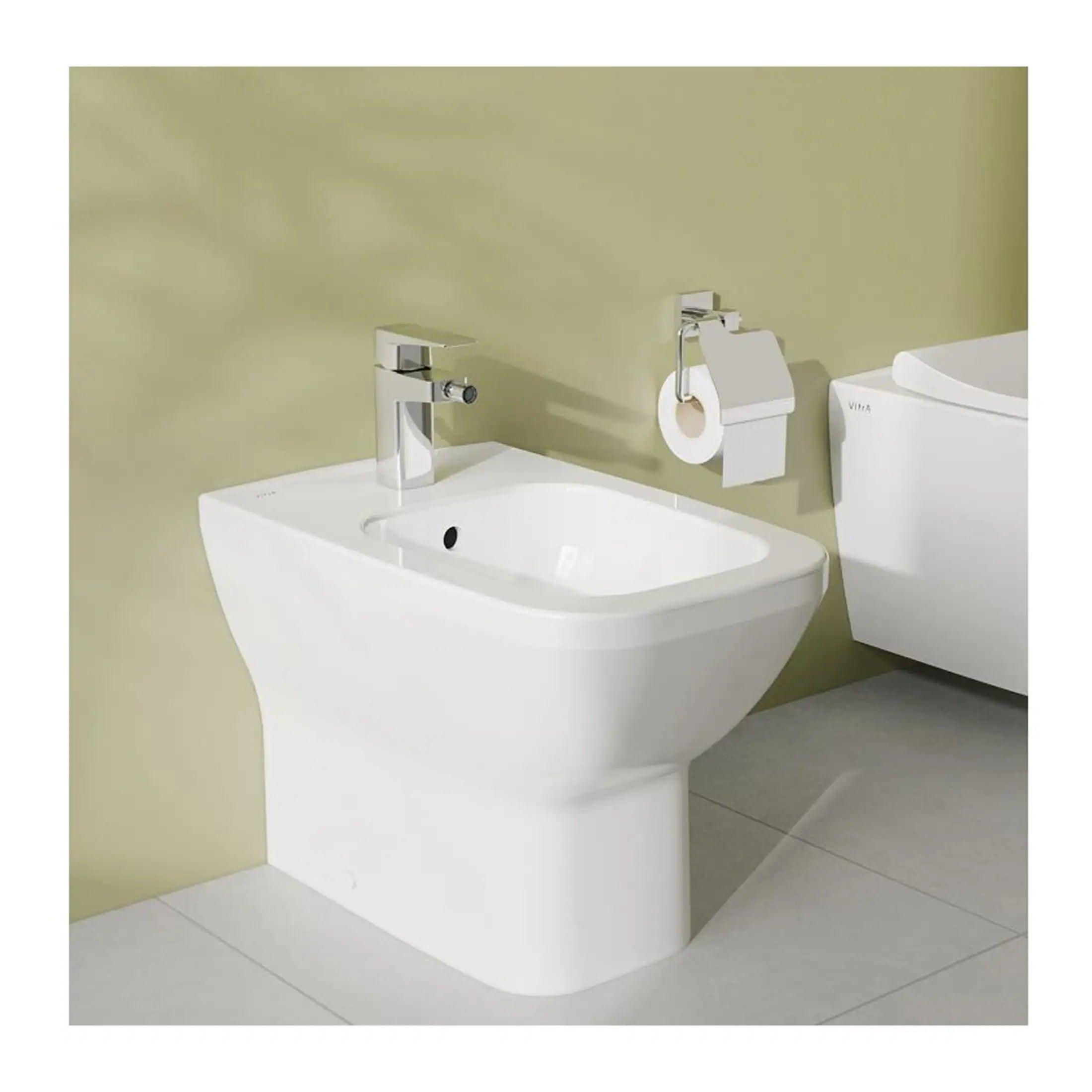 A modern white bidet with a sleek chrome faucet, positioned next to a toilet with a toilet paper holder on a light green bathroom wall, creating a contemporary and functional bathroom setup.