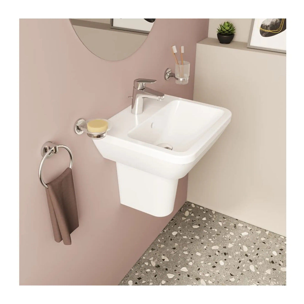 Contemporary white bathroom sink with modern chrome fixtures, wall-mounted soap dish and towel ring, against a soft pink wall with minimalist decor and terrazzo flooring, promoting stylish bathroom design.
