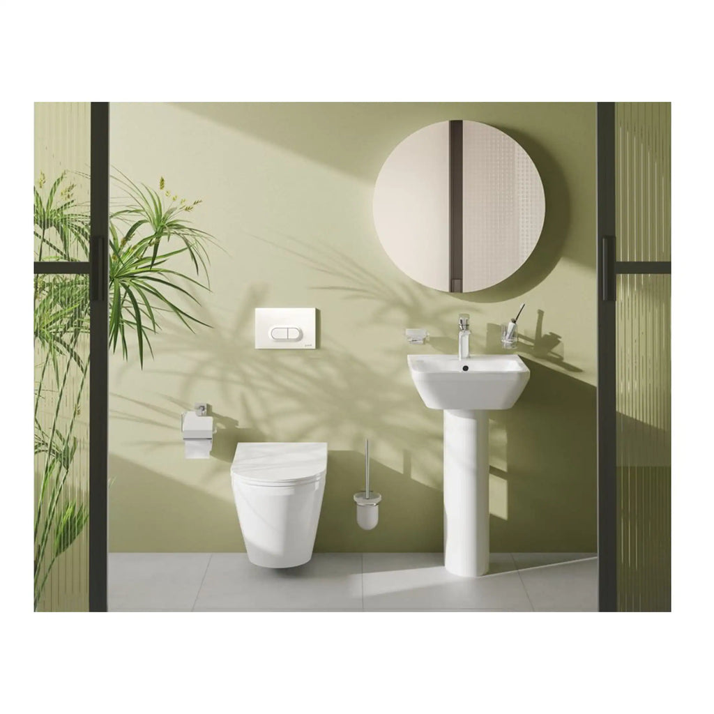 Contemporary bathroom featuring a white ceramic toilet, pedestal sink, round mirror, and modern fixtures, set against light green walls with natural plant accents, showcasing stylish and functional Bubly Bathrooms design.