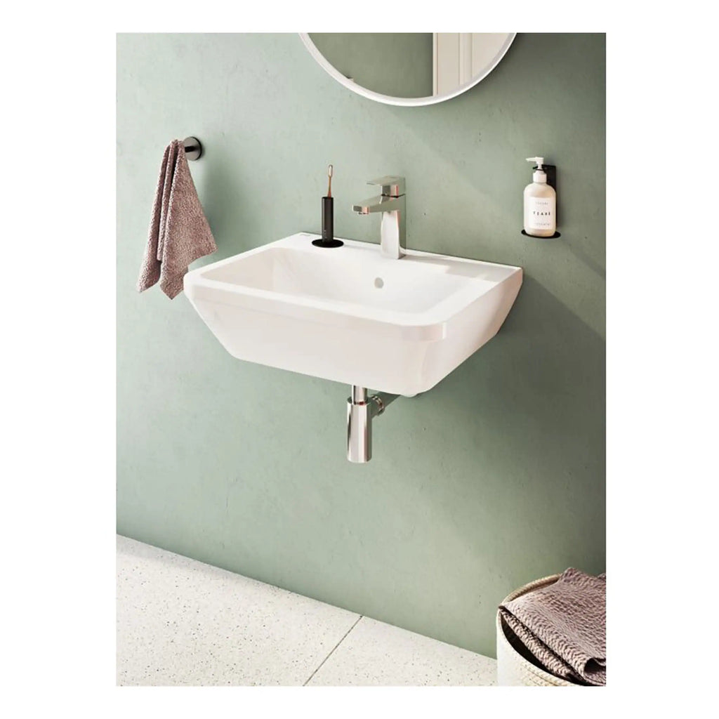 Modern wall-mounted bathroom sink with chrome fixtures and a pink towel hanging on a black wall hook, set against a soft green wall with a circular mirror.