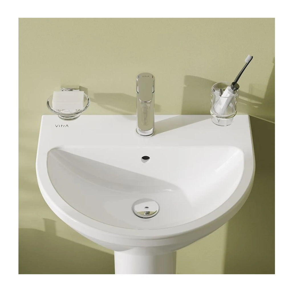 Sleek white bathroom sink with modern chrome faucet, soap dish, and toothbrush holder mounted on a soft green wall, designed for contemporary bathroom aesthetics and functionality.