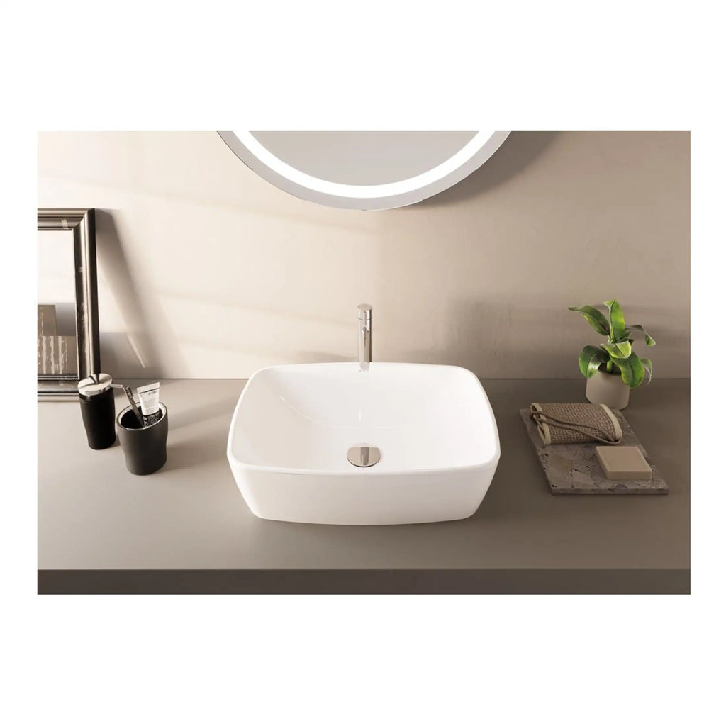 Sleek modern white bathroom basin with chrome tap, minimalist design, set on a grey countertop with bathroom accessories, plant, and mirror in the background, showcasing contemporary bathroom décor.