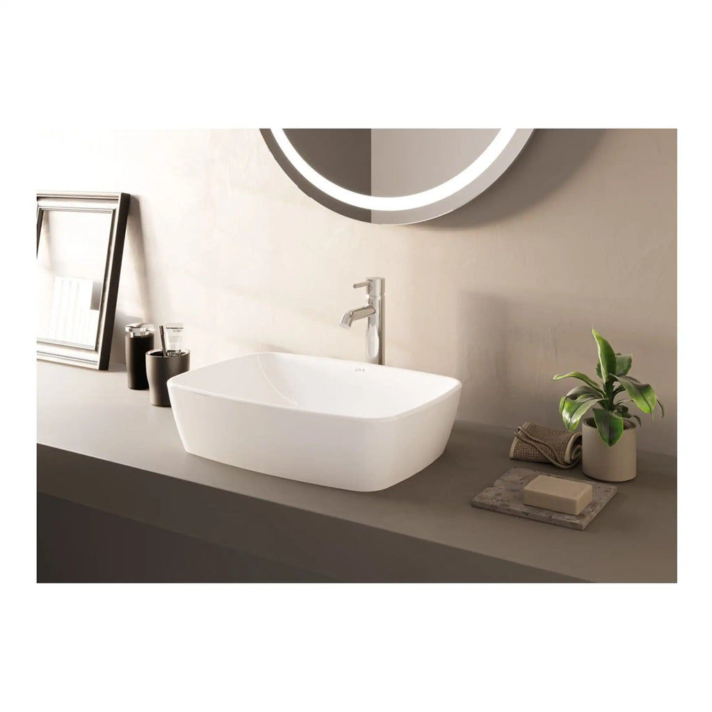 Sleek white bathroom basin with modern minimalist design, mounted on a neutral-toned countertop with contemporary fixtures, complemented by a round illuminated mirror, plant, and stylish accessories for a clean, elegant bathroom look.