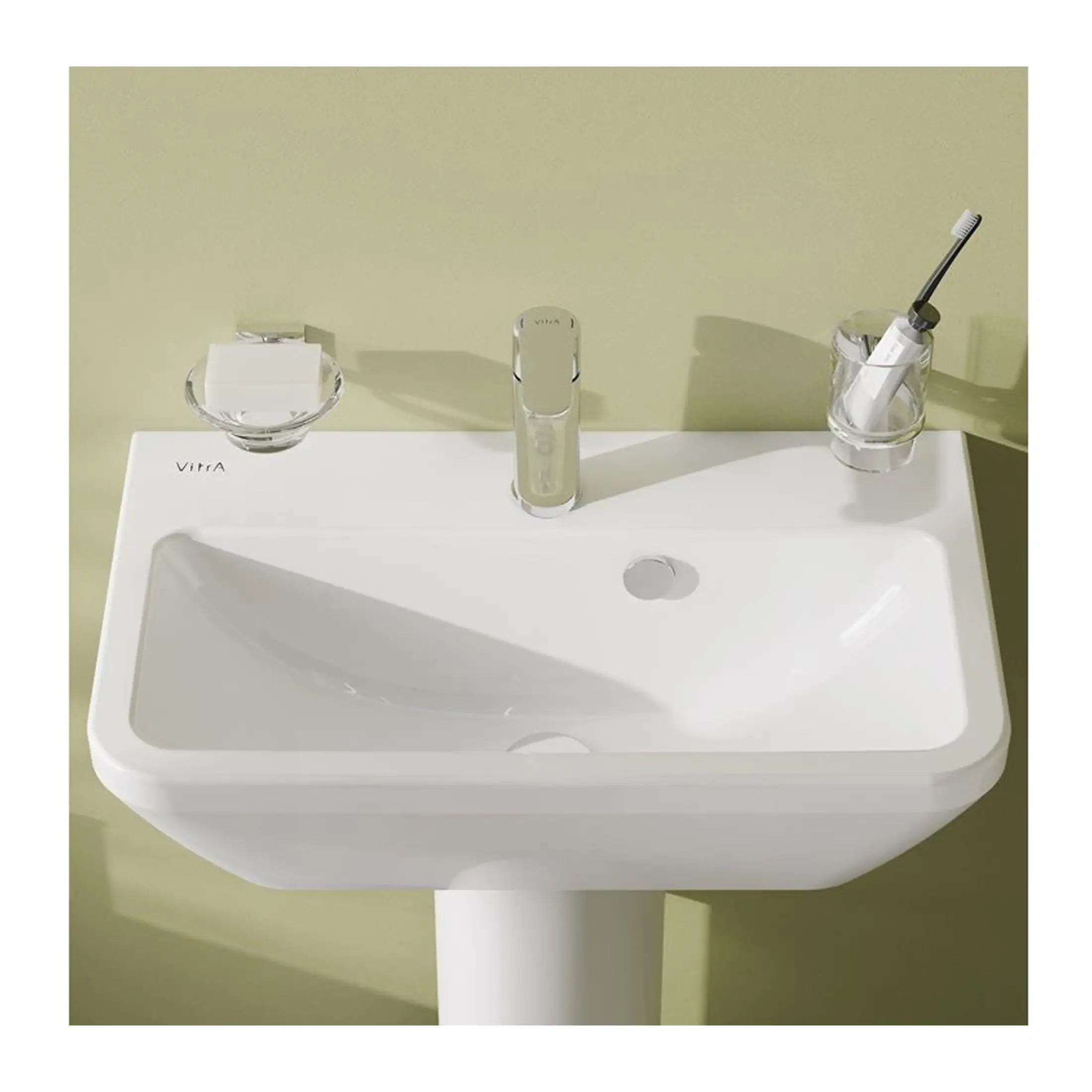 Shallow focus photo of white bathroom sink with a soap dish, toothbrush holder, and a sleek modern tap, set against a pale green wall, showcasing contemporary bathroom fixtures and design.