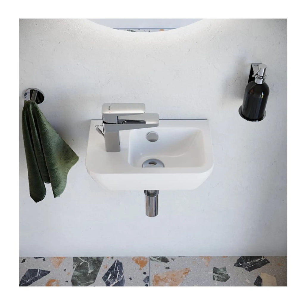 Modern white wall-mounted bathroom sink with chrome faucet, green hand towel hanging on side, black soap dispenser mounted on wall, with terrazzo floor; sleek, contemporary bathroom design.