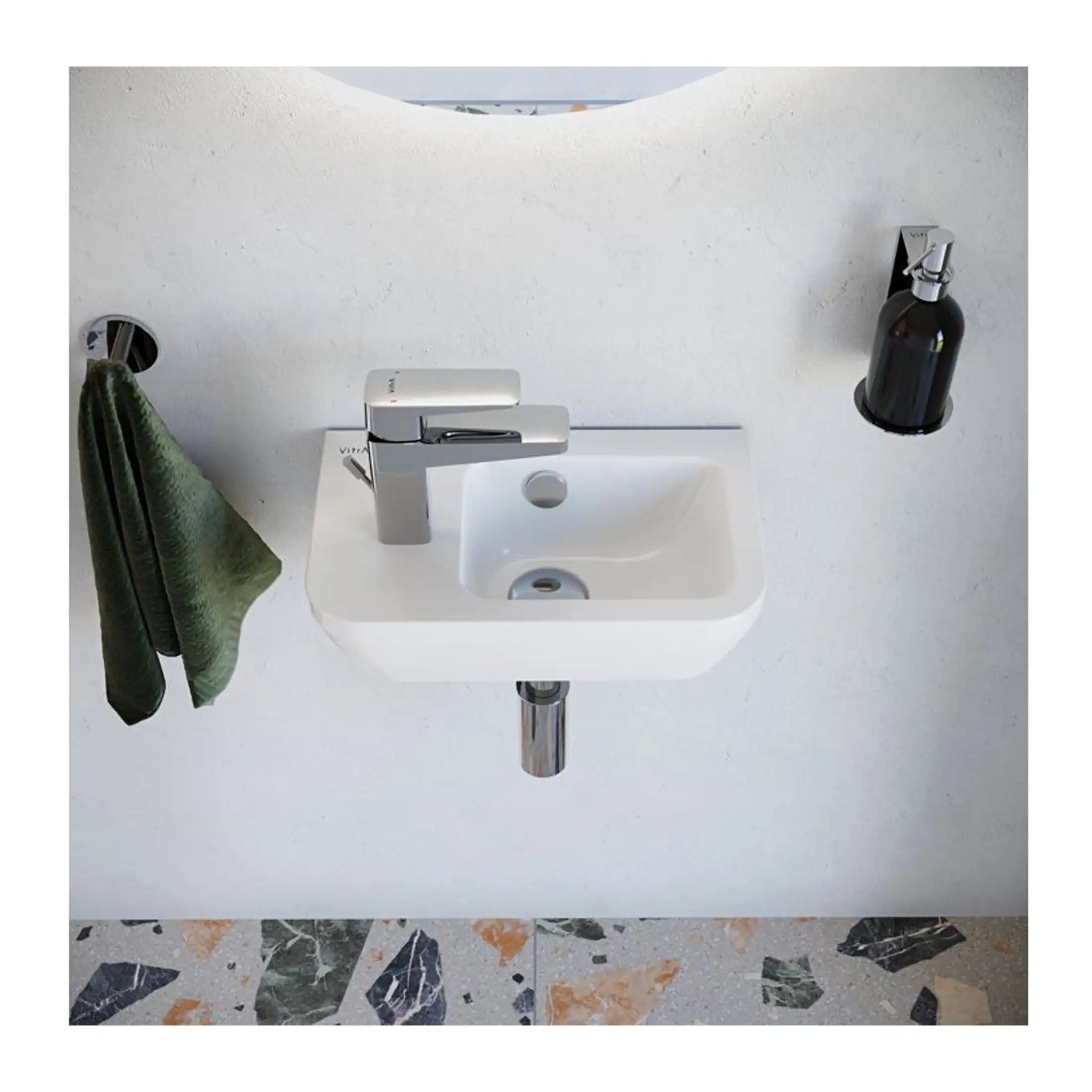 Modern white wall-mounted bathroom sink with chrome faucet, green hand towel hanging on side, black soap dispenser mounted on wall, with terrazzo floor; sleek, contemporary bathroom design.