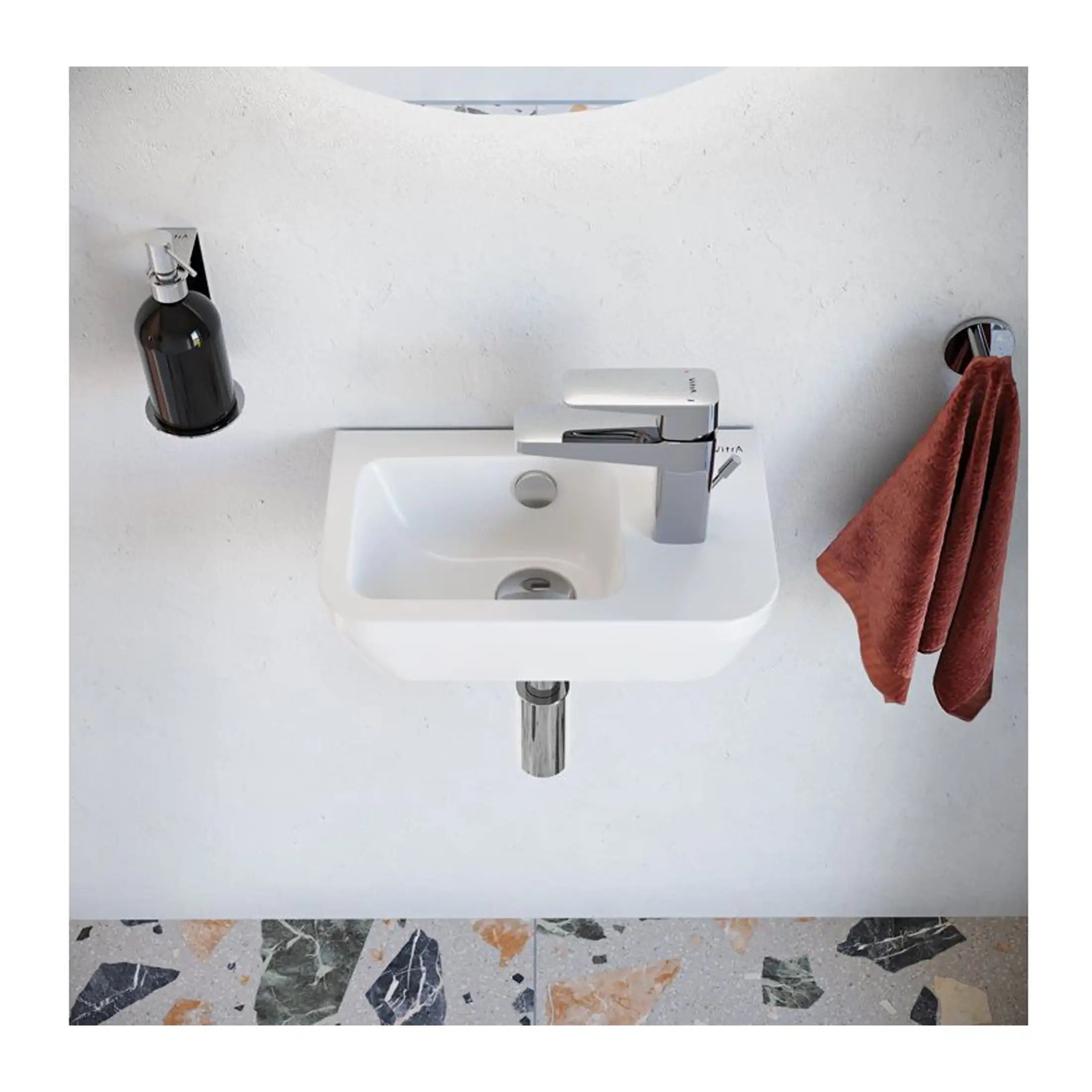 Small white bathroom sink with modern chrome faucet, mounted on wall with a black soap dispenser and rust-coloured towel hanging on the side, set against a plain white wall and terrazzo flooring.
