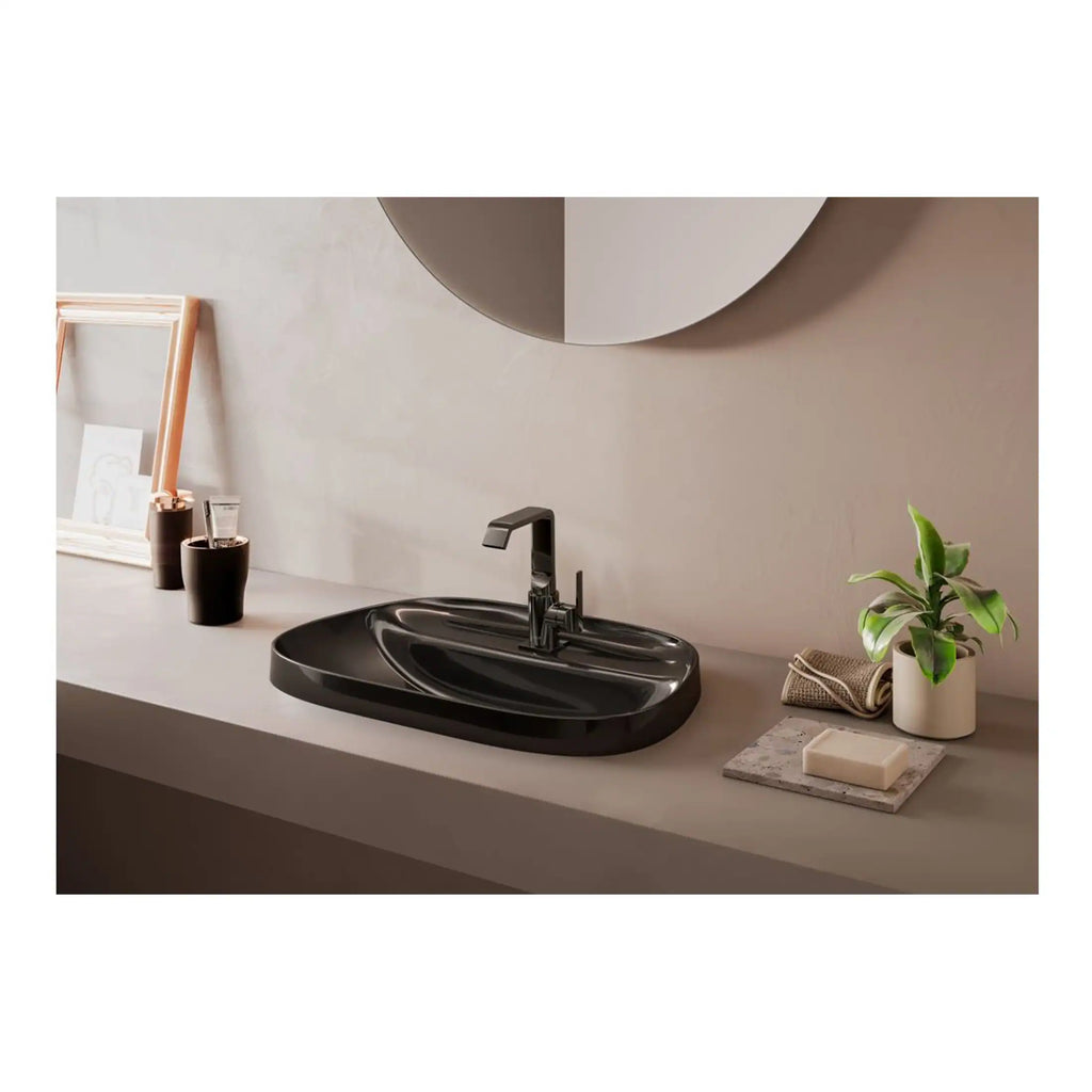 Smooth black bathroom sink with modern matte black faucet, minimalist decor, and green plant on neutral-toned vanity featuring stylish accessories for contemporary bathroom design.