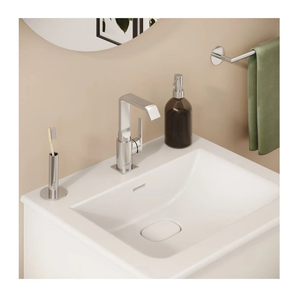 Elegant bathroom sink with modern chrome fixtures, soap dispenser, and toothbrush holder, complemented by a green towel on a sleek towel rail for a stylish bathroom decor.