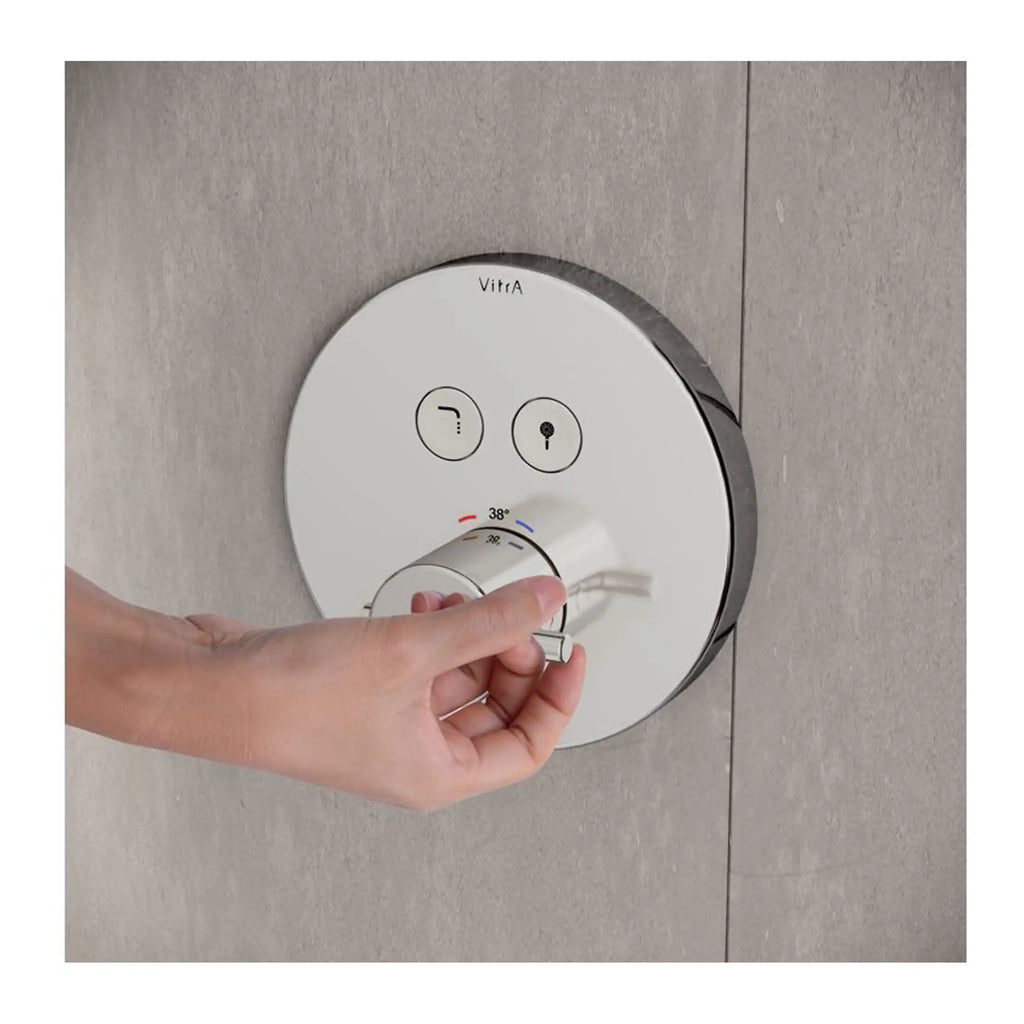 Vitra bathroom thermostat control panel with hand adjusting temperature, modern shower system, sleek white design, wall-mounted thermostat for precise temperature regulation in contemporary bathrooms.