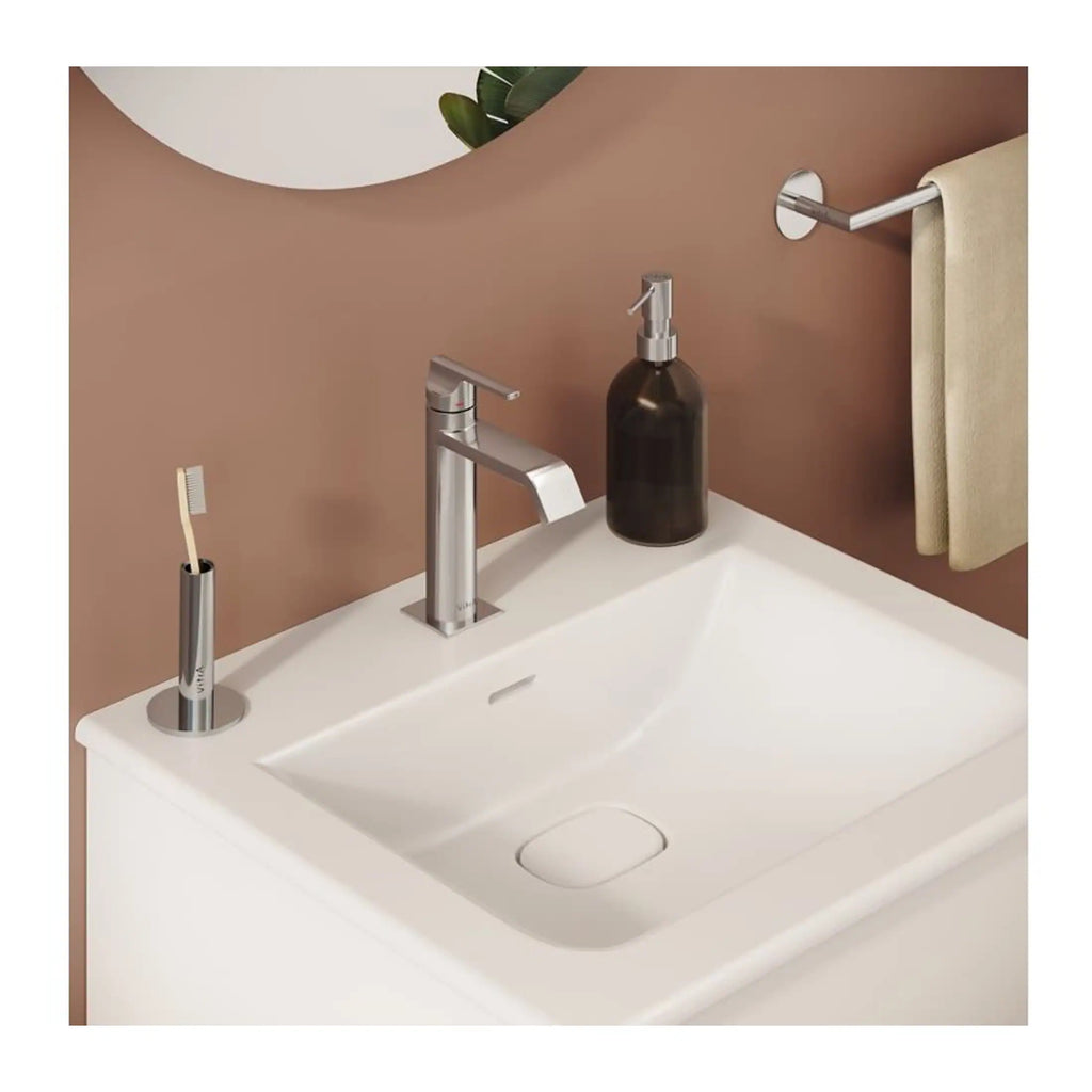 Toothbrush holder with toothbrush, modern bathroom sink with chrome tap, soap dispenser, beige towel on wall-mounted rail, stylish brown wall design, and minimalistic bathroom accessories from Bubly Bathrooms.