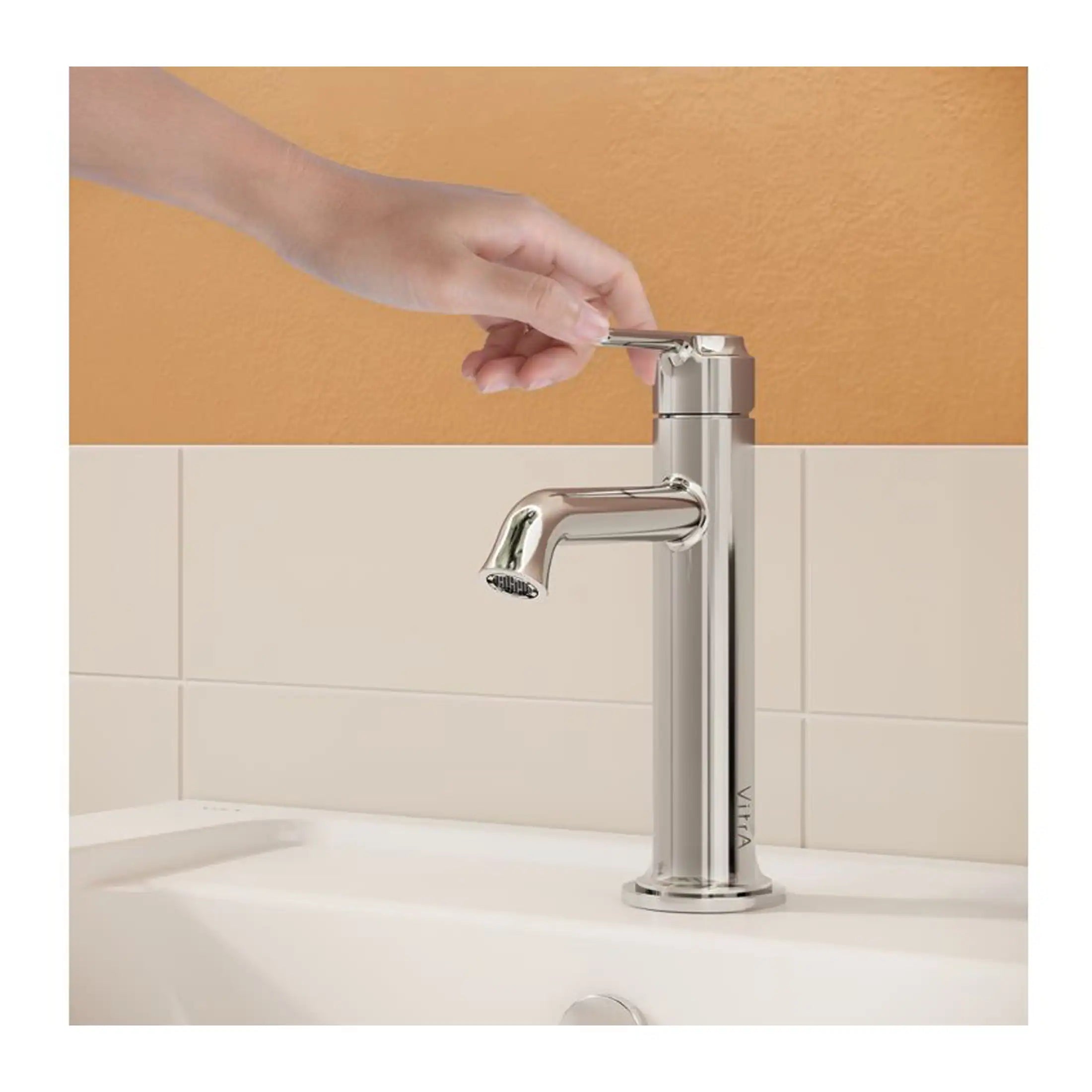 Sleek silver bathroom tap with a modern design, installed on a white sink against a warm beige and orange tiled wall, ideal for contemporary bathroom decor.