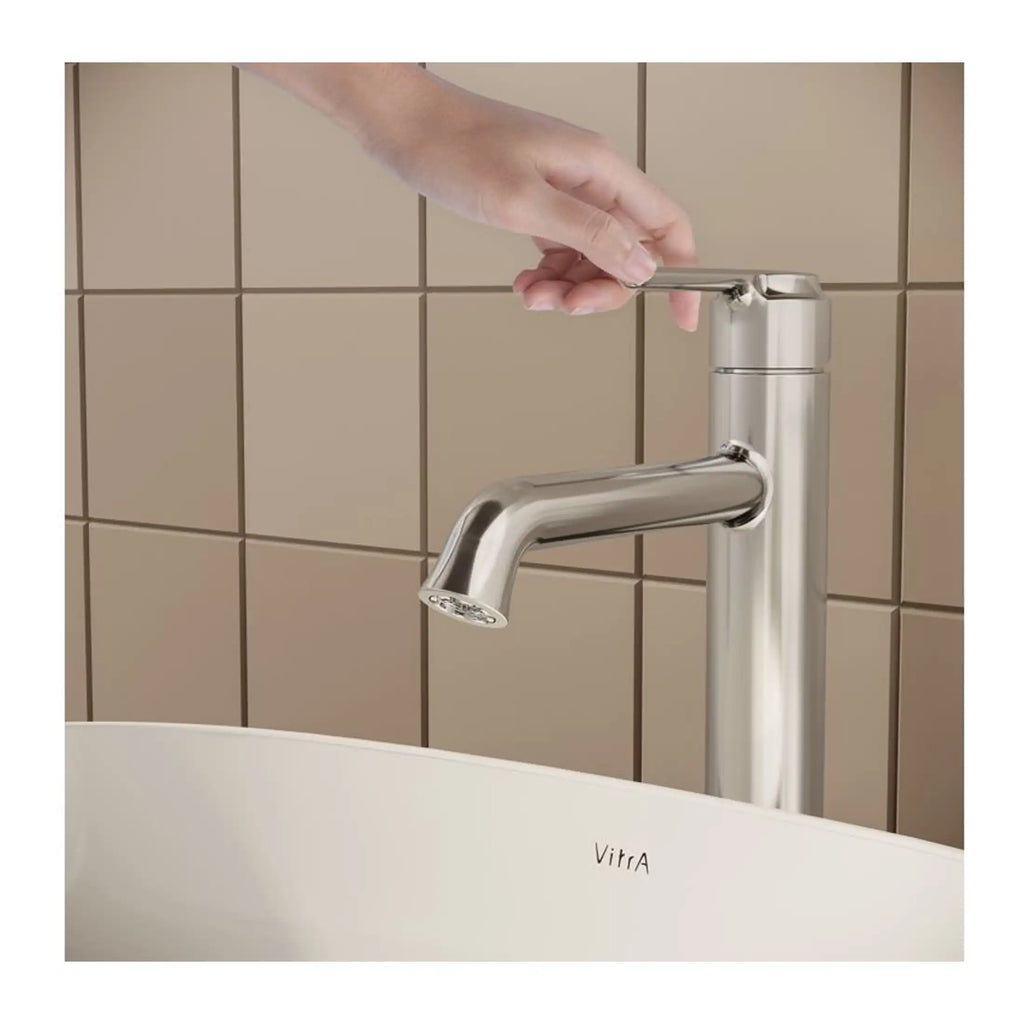 Sleek modern kitchen sink tap with a hand turning the tap handle, stainless steel finish, beige tiled wall background, contemporary bathroom fixtures, Bubly Bathrooms.