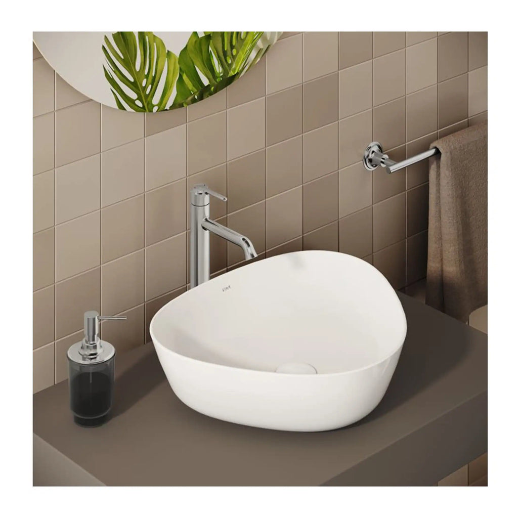 Sleek white bathroom vessel sink with modern chrome fixtures on a grey countertop, beige tiled wall, and green decorative leaves showcasing contemporary bathroom design.