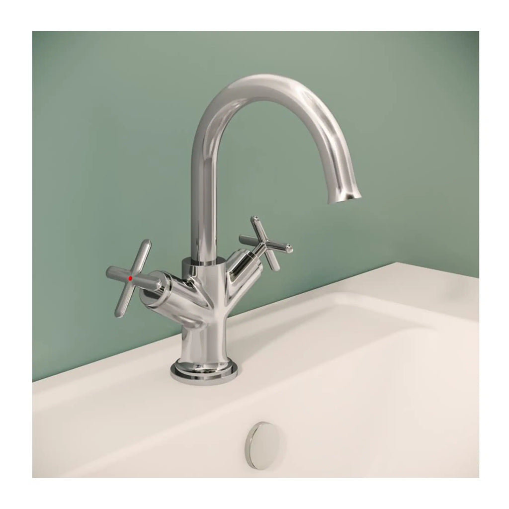 Shiny chrome kitchen or bathroom mixer tap with dual cross handles, installed on a white sink, against a pastel green wall, showcasing modern bathroom or kitchen fixture design.