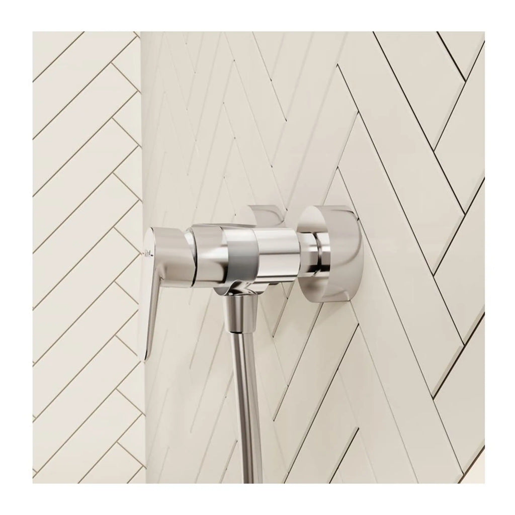Polished chrome bathroom flush valve with wall-mounted control lever on herringbone pattern tiled wall.