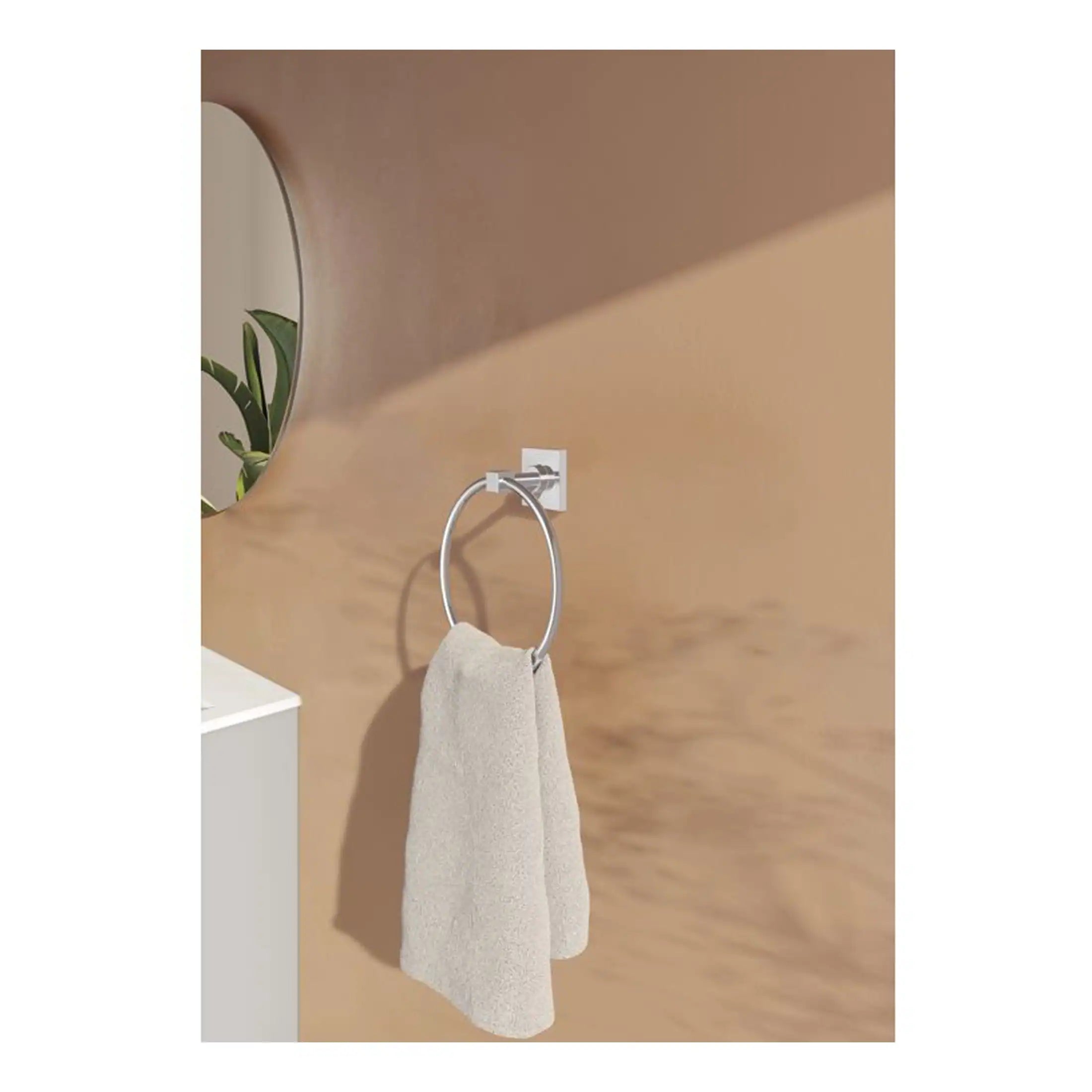 Minimalist towel ring attached to a beige wall with a cream towel hanging, modern bathroom decor, sleek design, perfect for contemporary bathroom spaces, complemented by a round mirror and green plant.