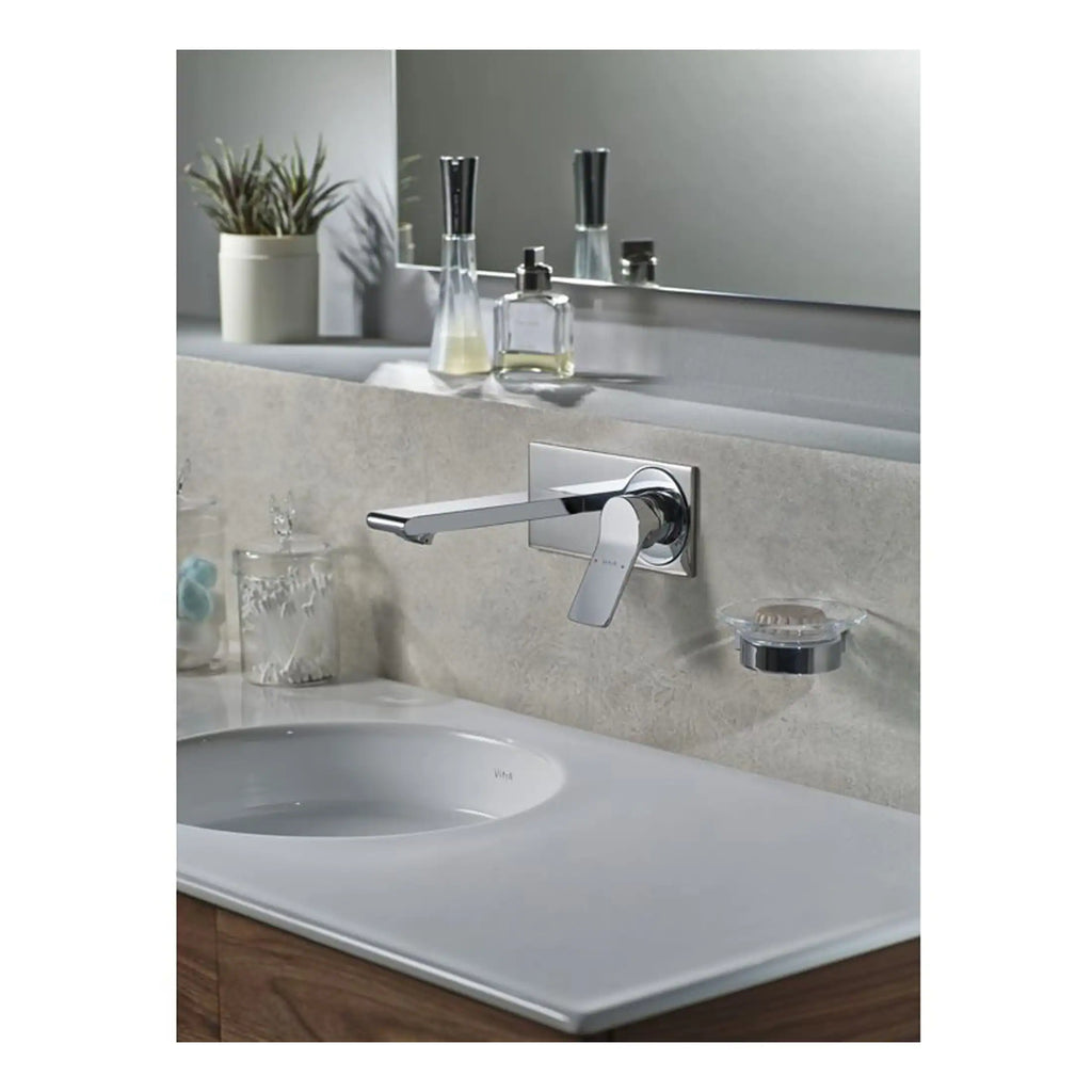 Sleek chrome bathroom tap mounted on beige stone countertop with mirror and toiletries in background.
