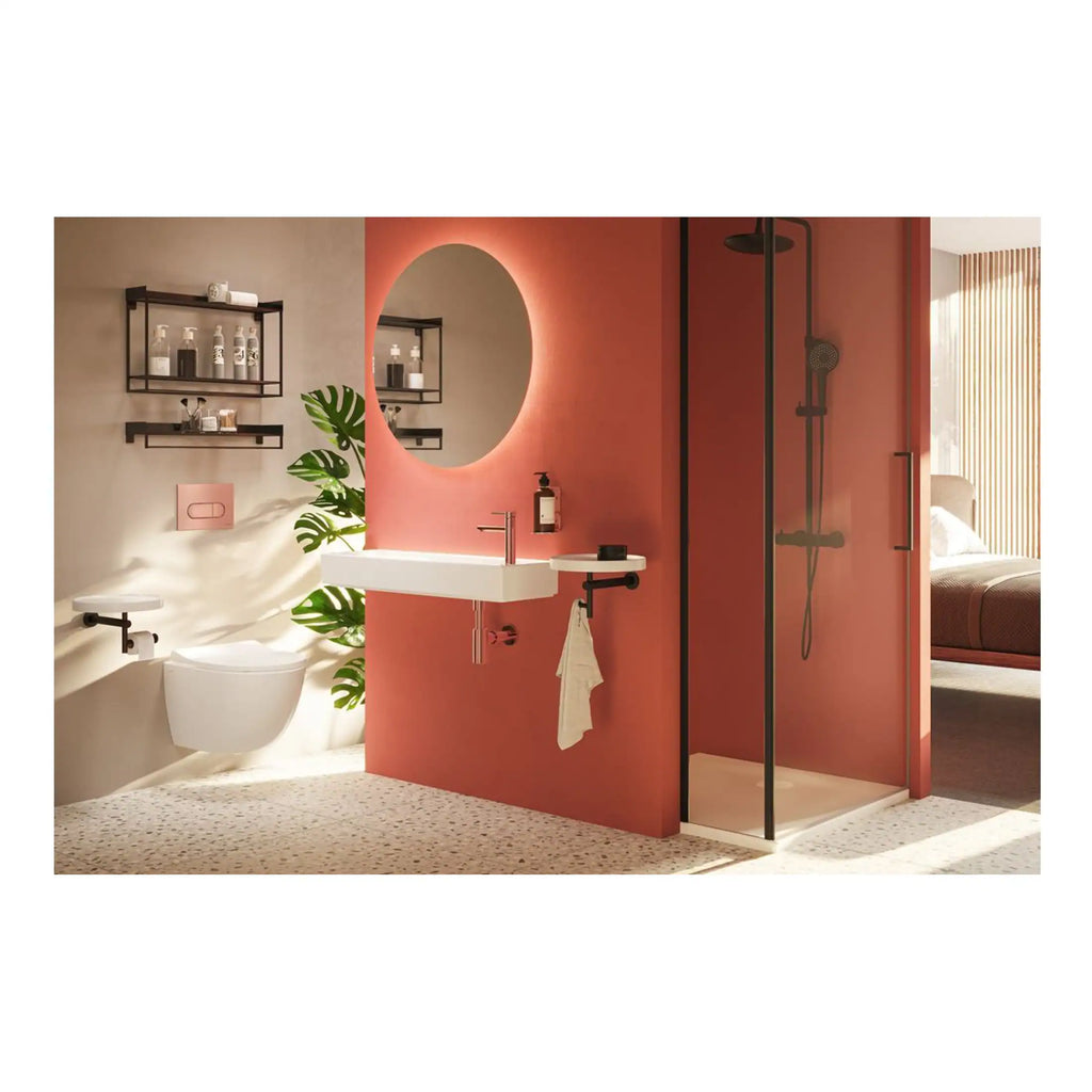 Stylish modern bathroom with a walk-in shower, white wall-mounted toilet, round mirror with backlit LED, black metal shelving, coral wall, and natural light creating a contemporary and inviting space.