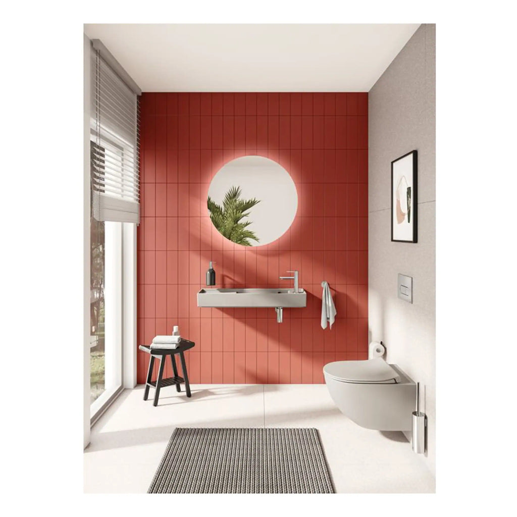 Bright modern bathroom with a floating sink, circular mirror with backlighting, wall-mounted toilet, and large window with blinds, featuring a stylish red tiled accent wall and minimalistic decor.