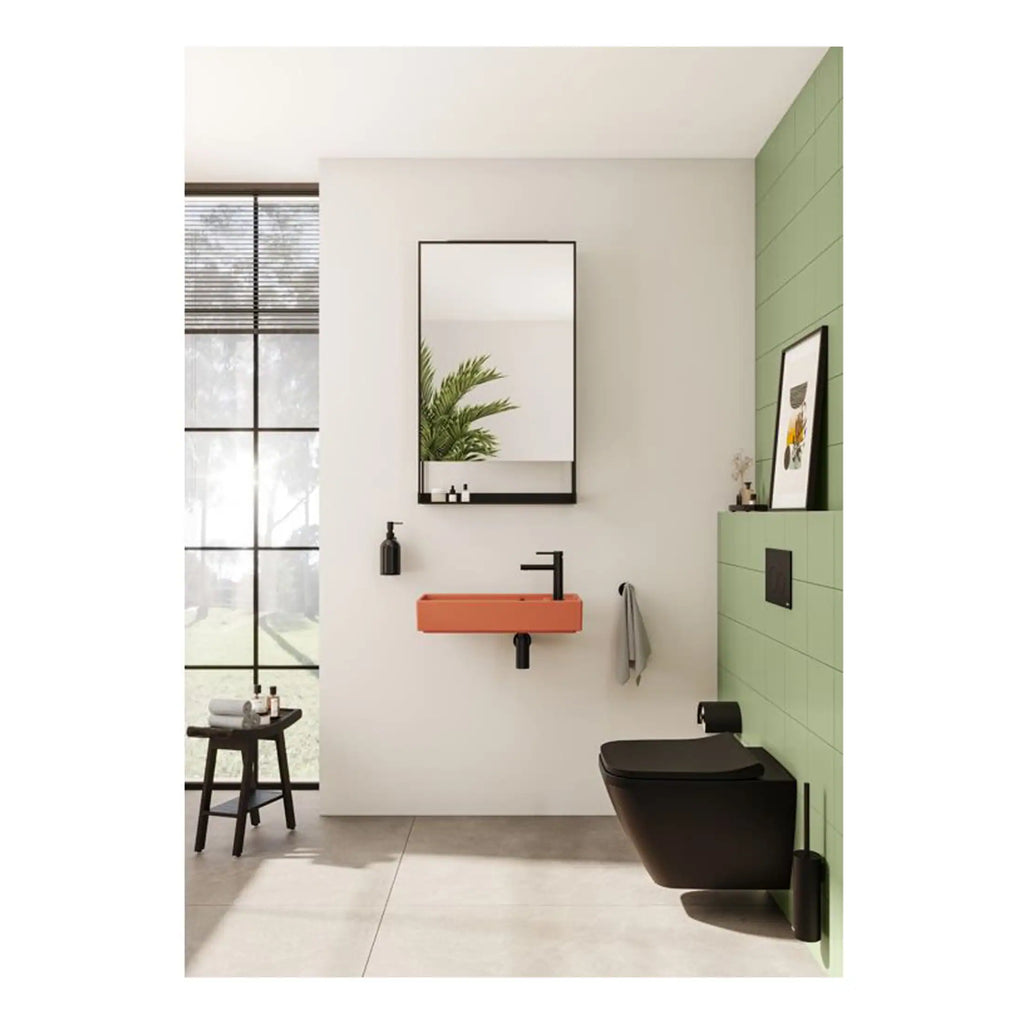 Vibrant orange bathroom sink with modern black fixtures, adjacent to a sleek black toilet on a green tiled wall, featuring a minimalist mirror and natural light, perfect for contemporary bathroom design.