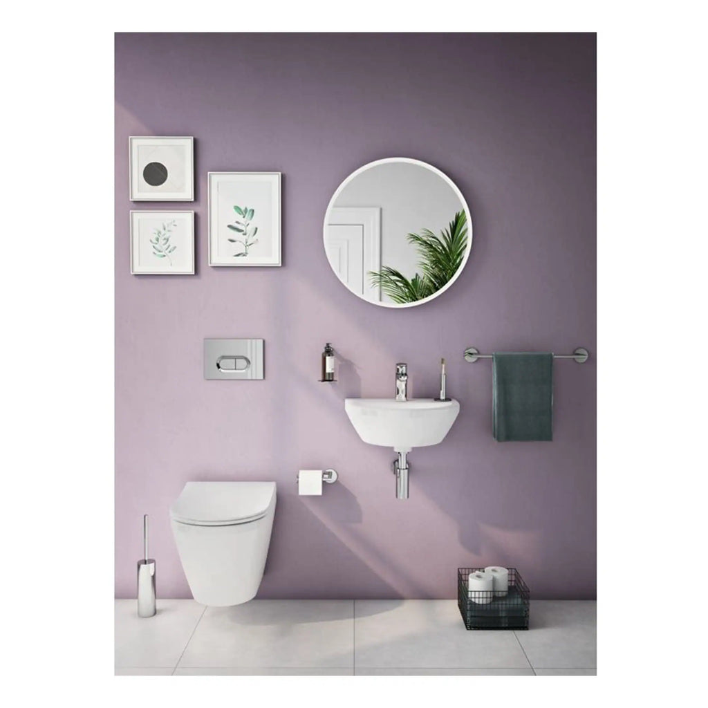 Sleek modern bathroom with lavender wall, wall-mounted toilet, compact sink with chrome faucet, round mirror, framed botanical artwork, plush towel, and black storage basket with toilet paper.