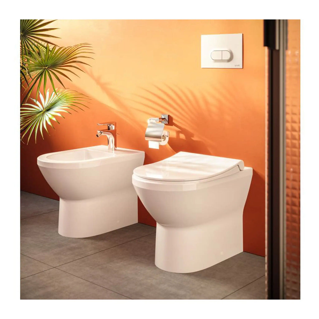 Sleek white bidet and toilet with modern fixtures in a contemporary bathroom setting, featuring a vibrant orange wall, lush green plant, and a concealed cistern for a stylish, space-saving design.