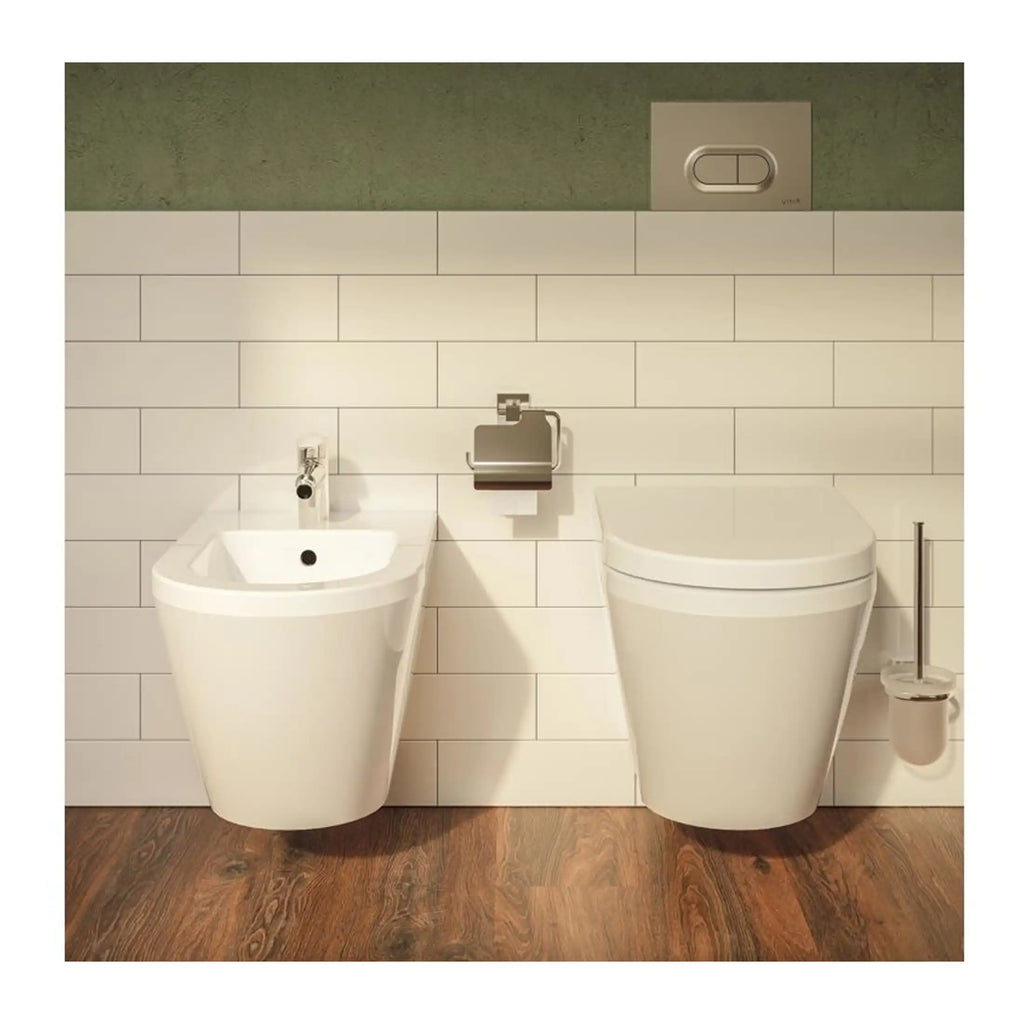 Bubly Bathrooms modern white bidet and toilet set with wall-mounted flush buttons, stainless steel toilet paper holder, and wooden flooring, showcasing stylish bathroom design elements.