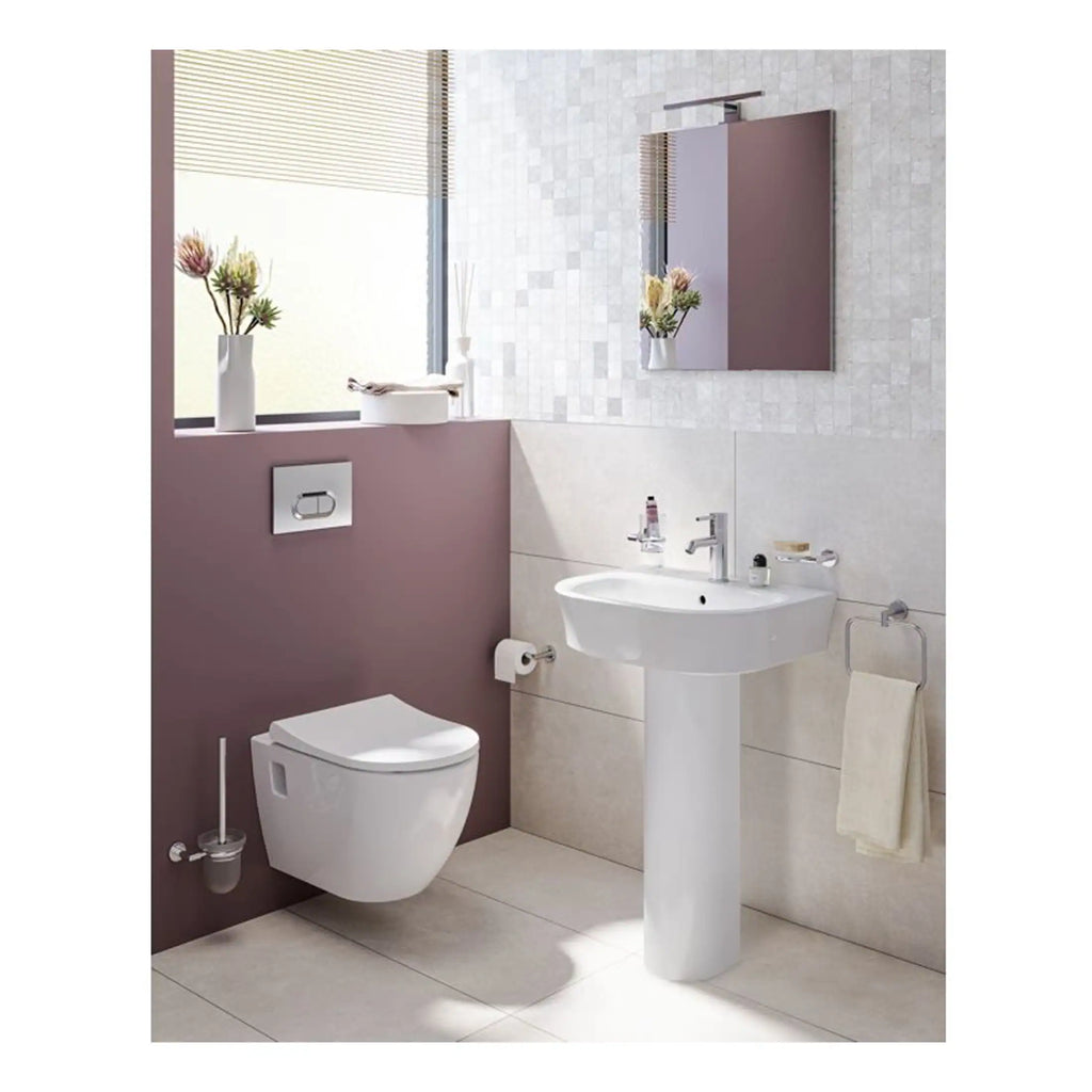 Minimalist bathroom with modern white toilet, ceramic pedestal sink, and stylish wall-mounted mirror, featuring soft pink and neutral tiled walls, lush decorative vases, and natural light for a calming, contemporary space.