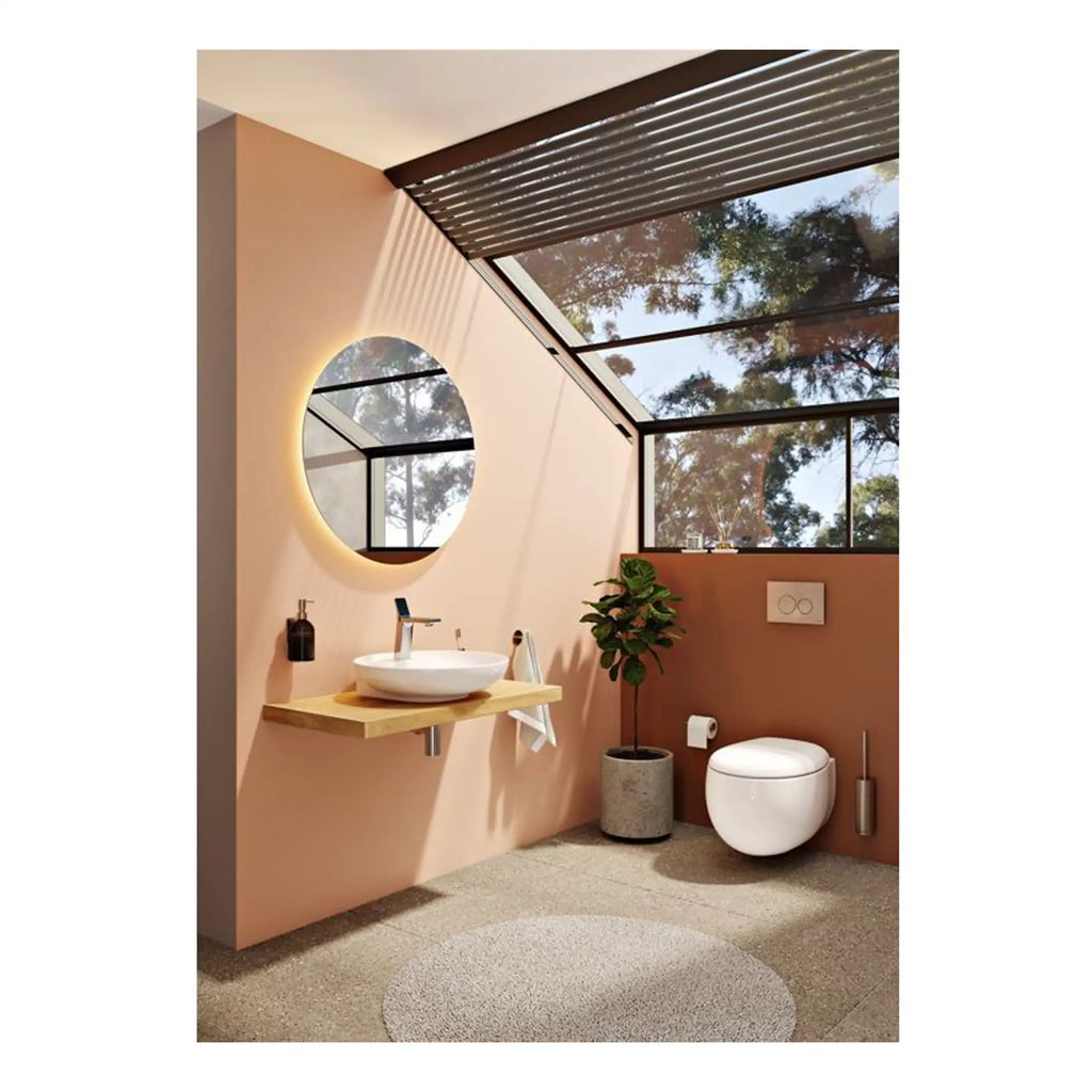 Sleek modern bathroom with a wall-mounted toilet, round mirror with backlighting, and a floating wooden vanity with a vessel sink, decorated with indoor plants and natural light from large glass windows, designed for comfort and style.