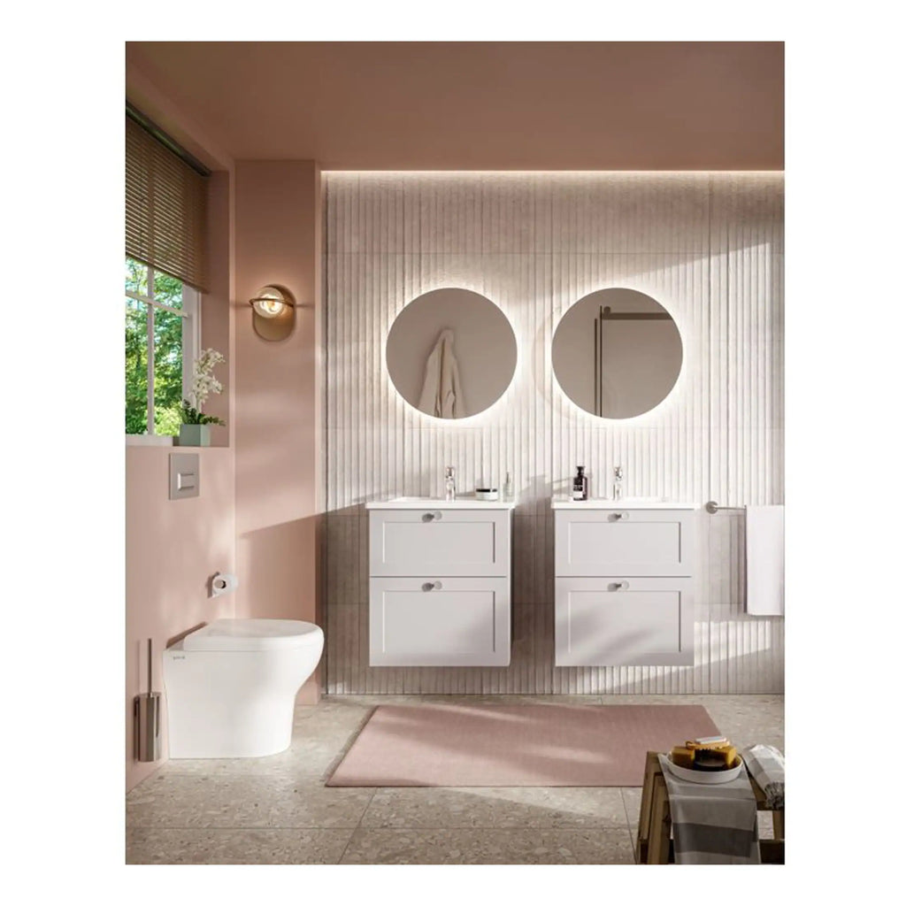 Elegant modern bathroom with dual white vanities, round backlit mirrors, wall-mounted toilet, soft pink walls, and minimalist decor, creating a serene and stylish space.