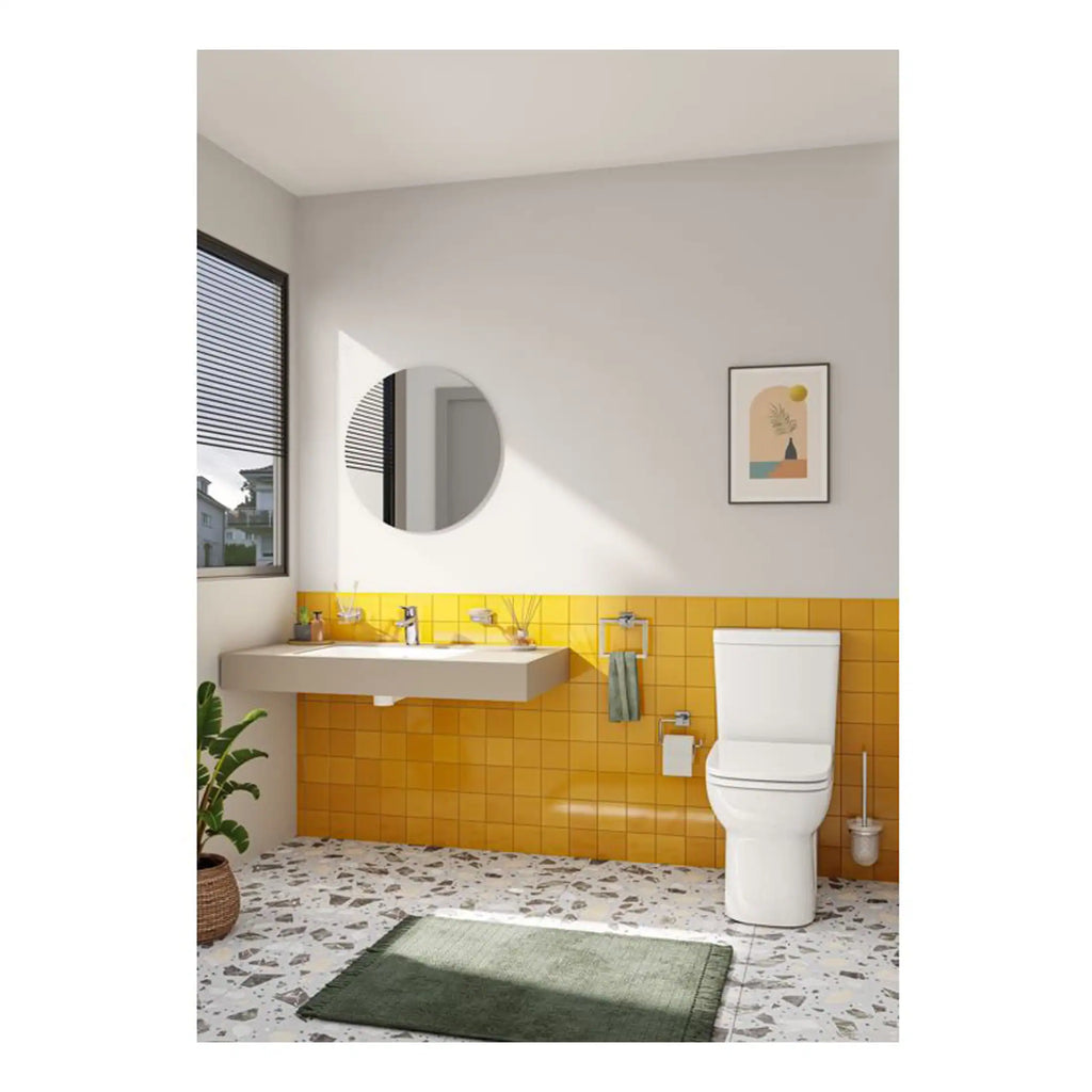 Bright modern bathroom featuring a white toilet, yellow tiled wall, wall-mounted sink with accessories, circular mirror, colourful artwork, terrazzo flooring, and a green bath mat, perfect for contemporary bathroom design.